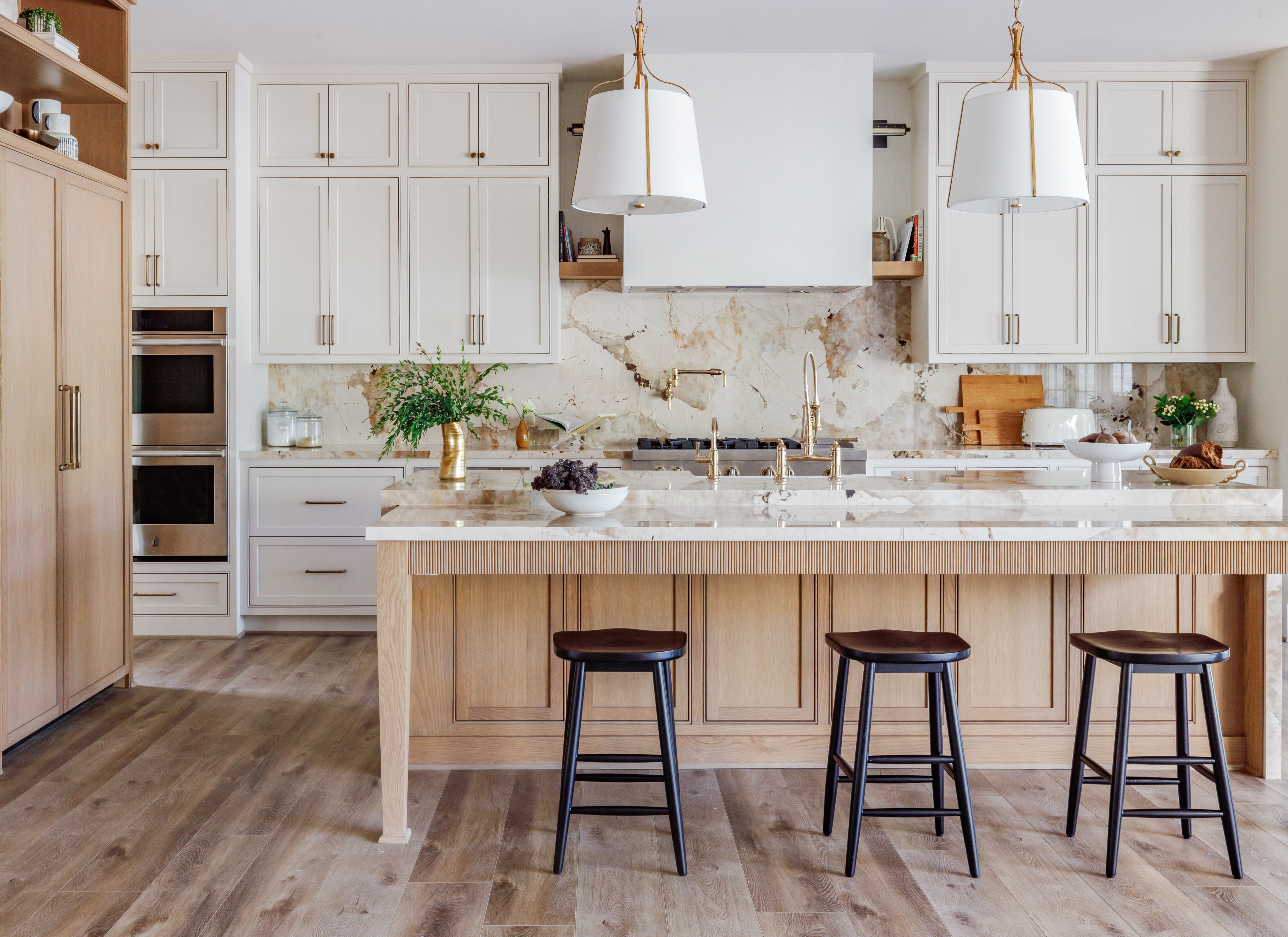 Custom kitchen with a large center island, natural wood cabinetry, marble backsplash, brass fixtures, and layered lighting that balances luxury and function.