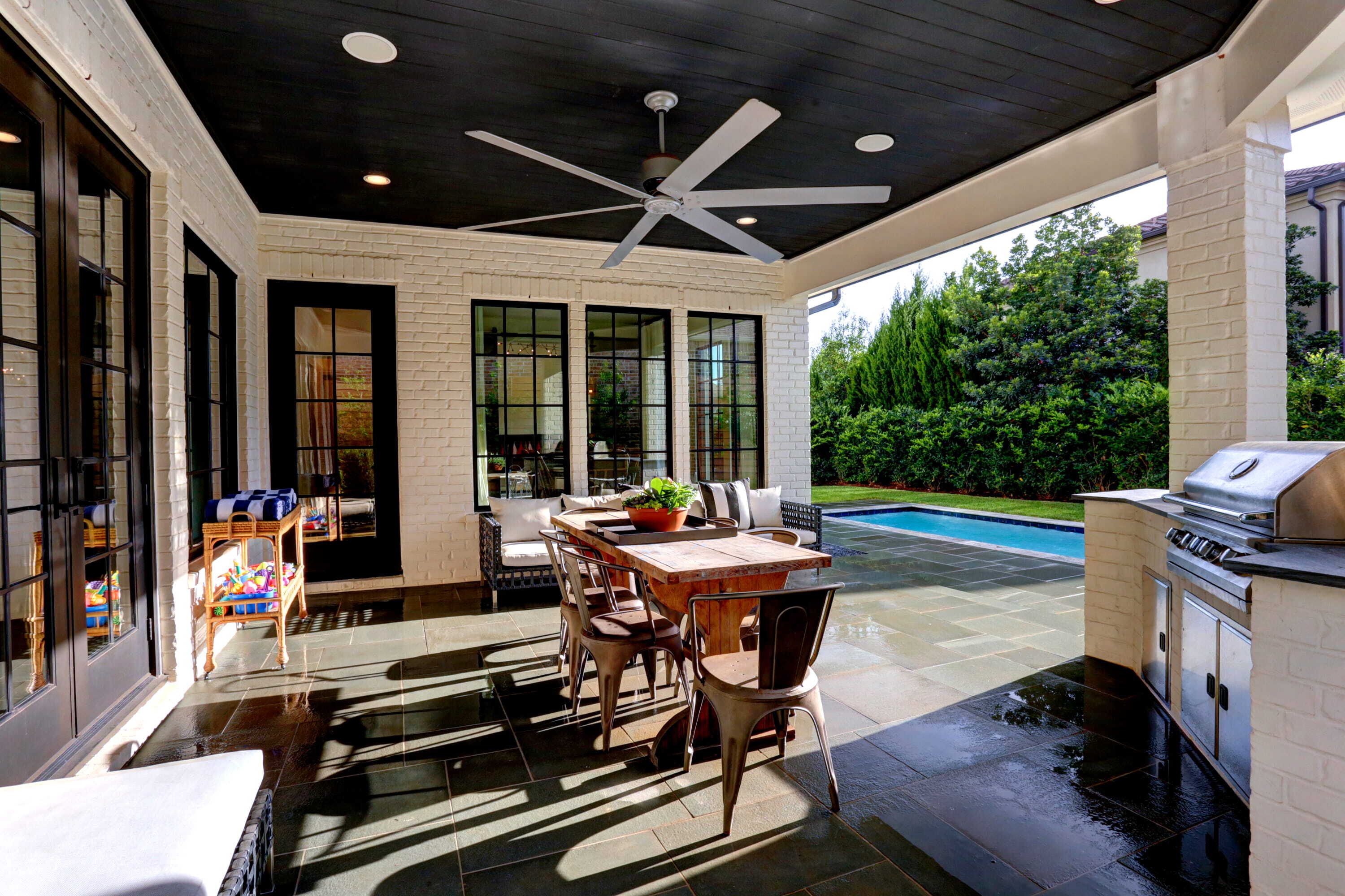 Covered outdoor living area with dining space, summer kitchen, pool, and family-friendly patio design