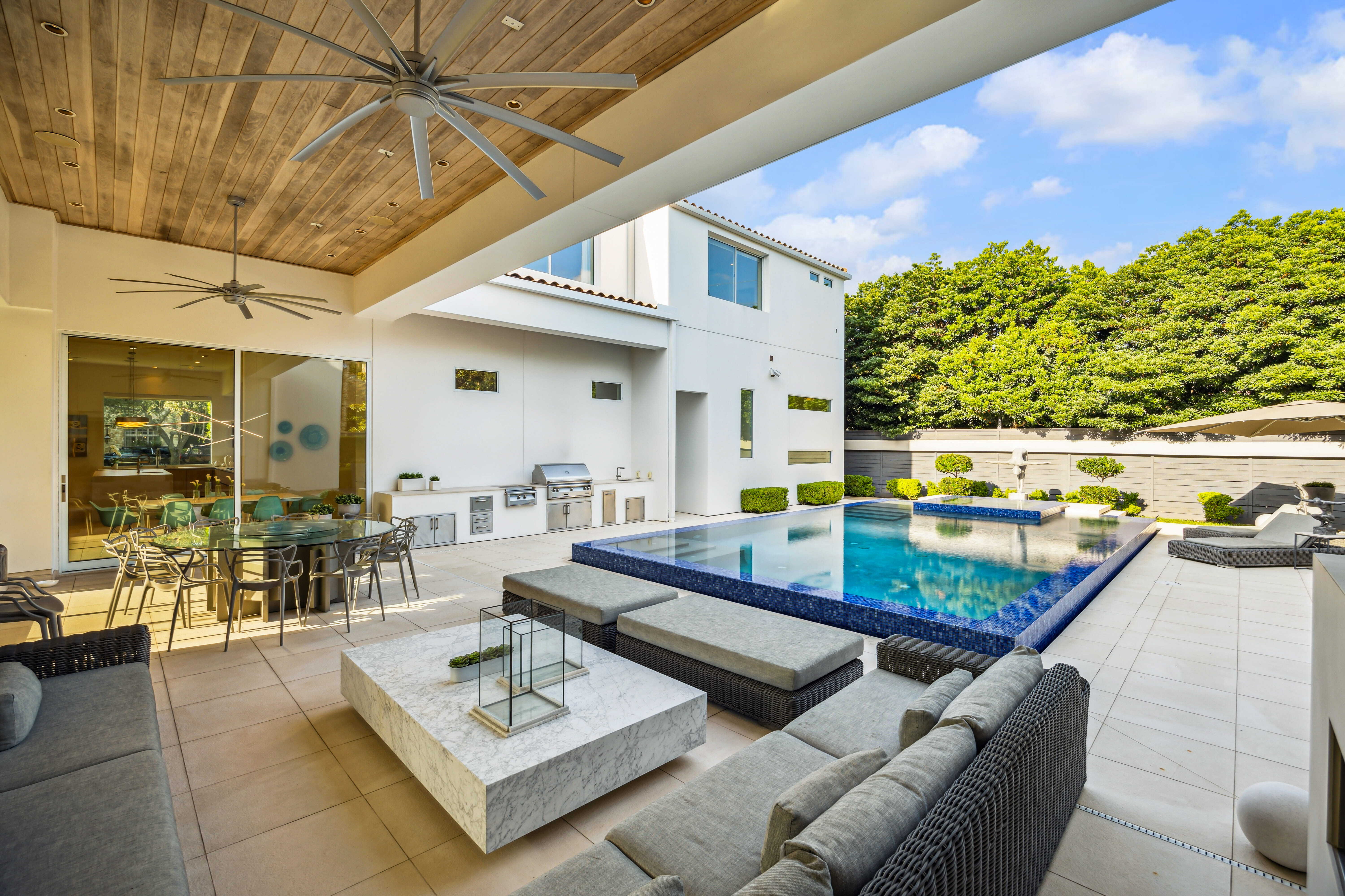 Covered patio with outdoor kitchen, pool, lounge seating, and seamless indoor-outdoor living