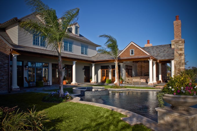 Sims Builders Houston coastal Southern custom home with white columns, palm trees, covered wraparound porch, and winding dark-bottom pool