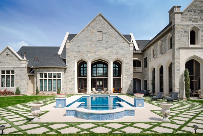 Sims Builders Houston Gothic-inspired stone custom home with pointed arch windows, mosaic blue tile pool and spa, and diamond-pattern stone patio