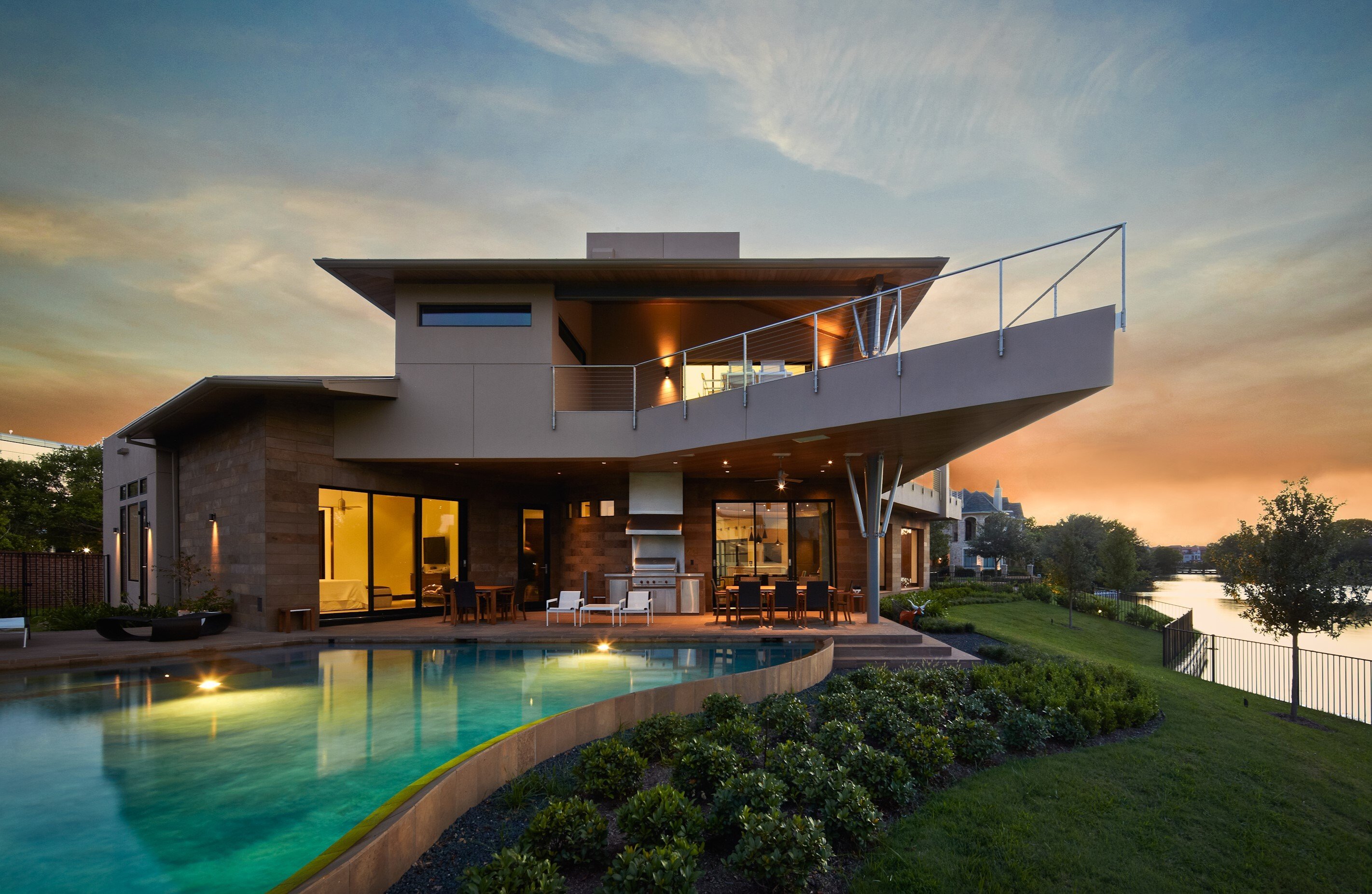 Sims Builders Houston modern contemporary custom home with cantilevered upper deck, cable railings, outdoor kitchen, and curved infinity pool at sunset
