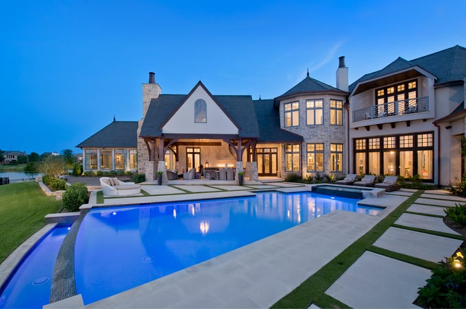 Sims Builders Houston transitional European custom home with timber frame covered porch, outdoor kitchen, and large illuminated pool at blue hour