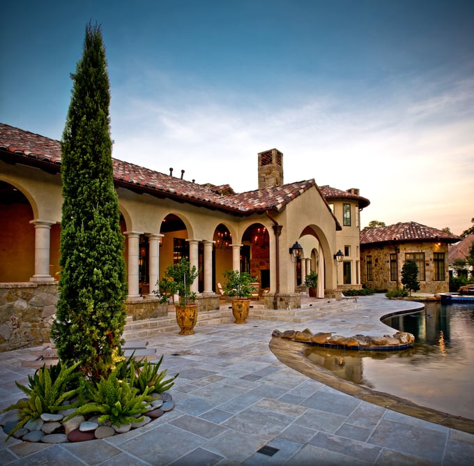 Sims Builders Houston Tuscan Mediterranean custom home with stone columns, arched loggia, Italian cypress tree, and travertine pool patio at dusk