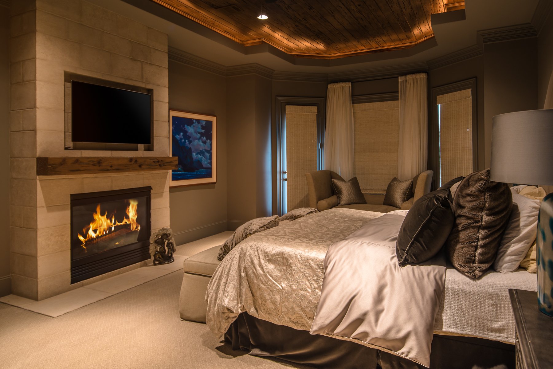 Renovated primary bedroom with fireplace, wood ceiling detail, custom millwork, and layered neutral finishes.