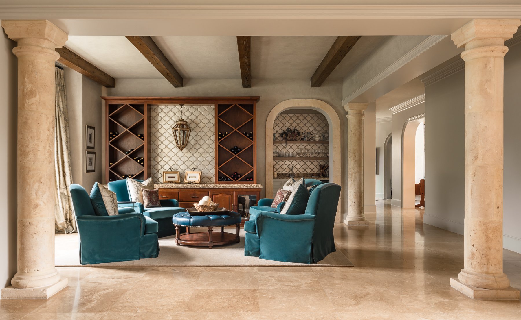 Renovated luxury home living space with custom wine storage, arched openings, stone columns, and built-in cabinetry.