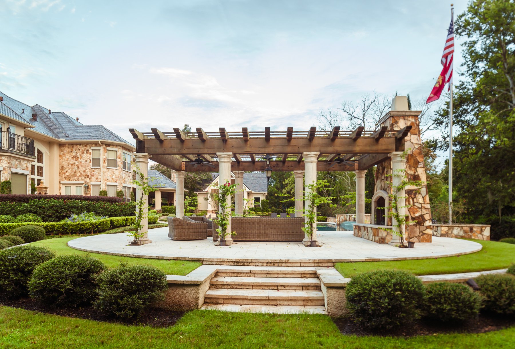 Luxury outdoor living area with pergola, stone columns, landscaped grounds, and poolside entertaining space.