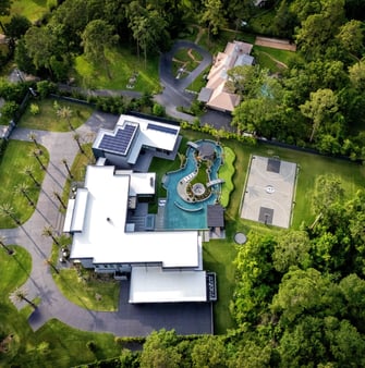 Aerial view of modern luxury Houston estate featuring resort-style pool with lazy river, spa, swim-up pavilion, landscaped grounds, and private basketball court beside the contemporary custom home.