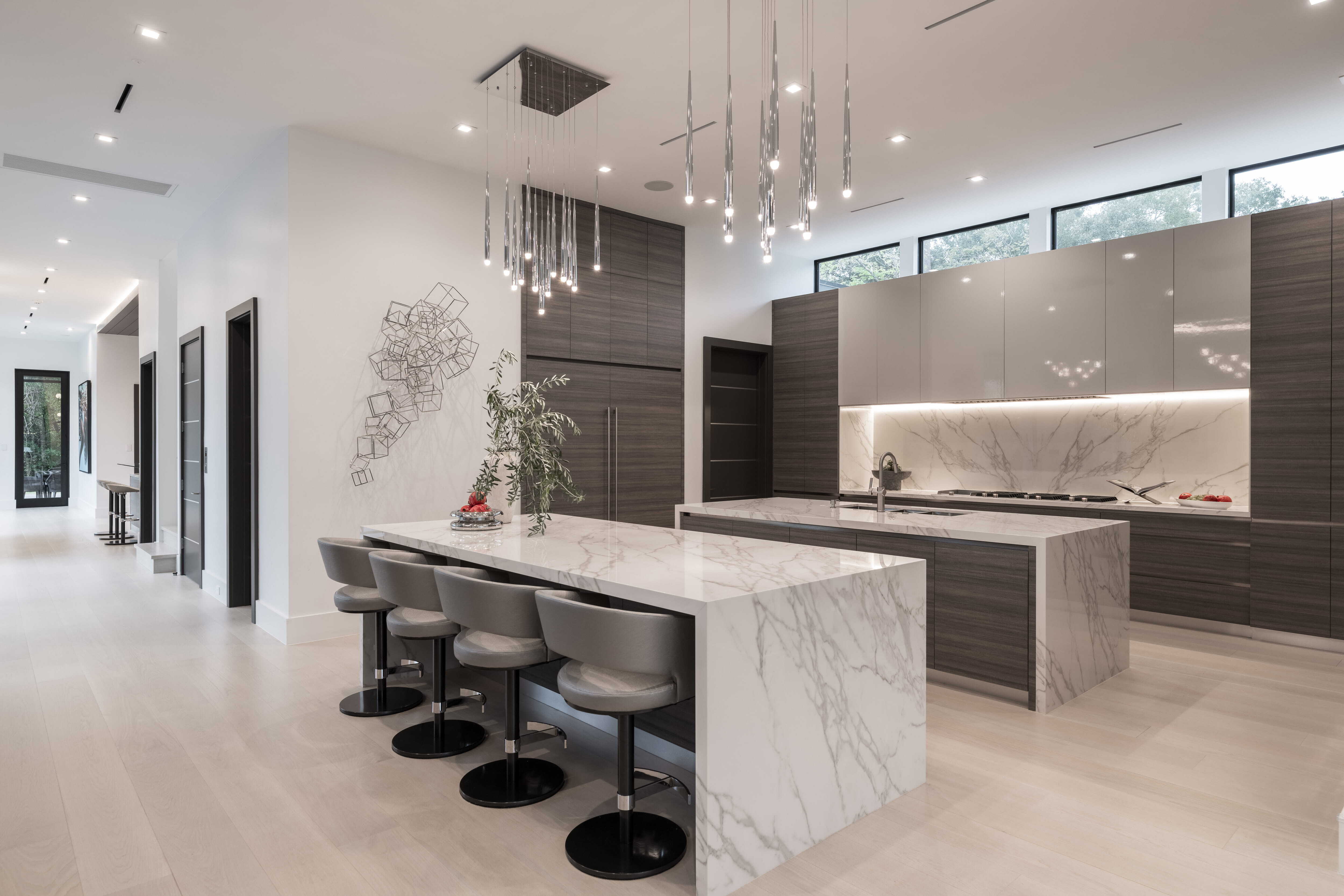 Modern kitchen with oversized marble waterfall island, sculptural pendant lighting, sleek wood cabinetry, and open-plan layout designed for entertaining in a luxury Memorial Houston custom home.