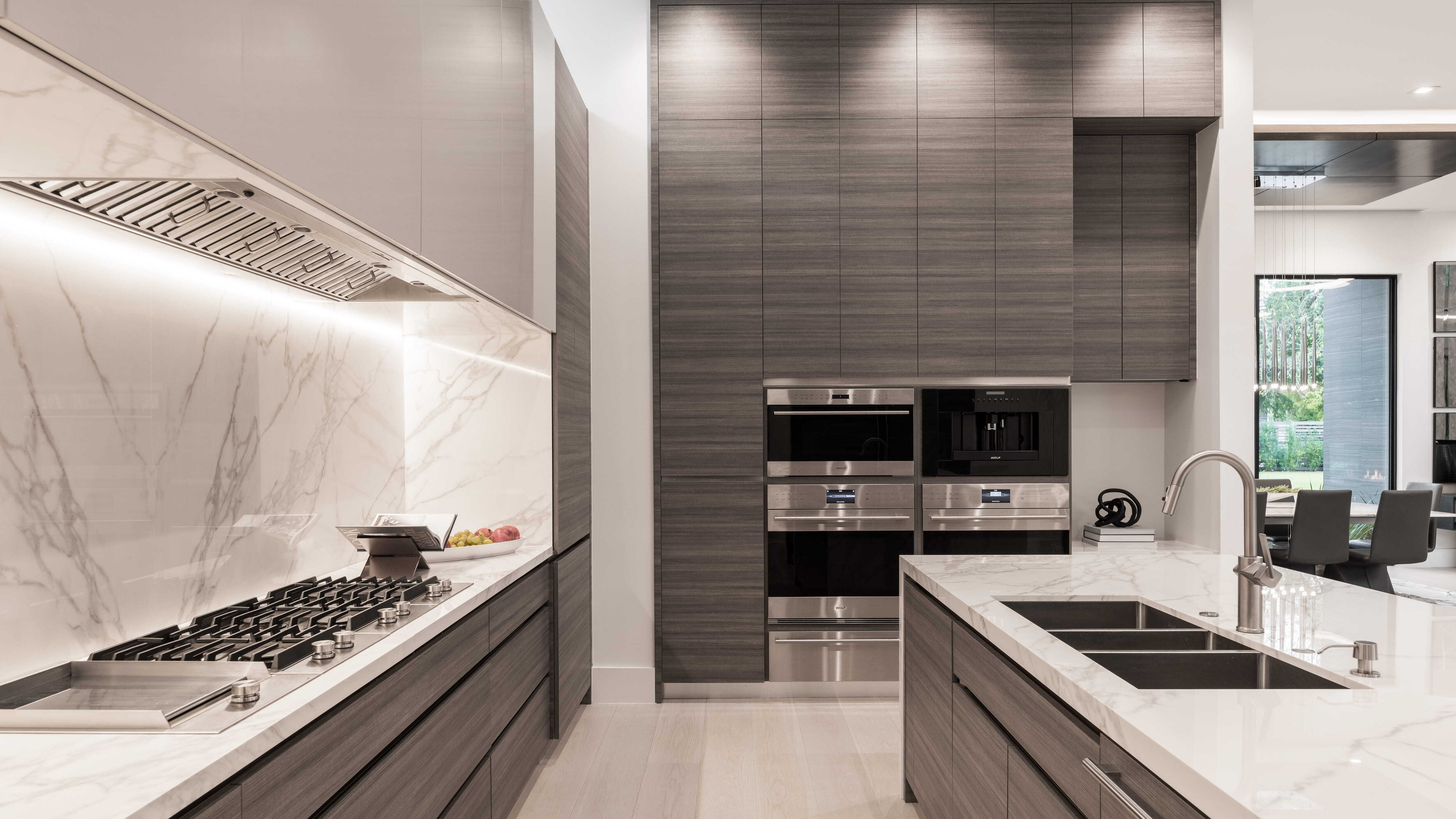 Contemporary kitchen with marble waterfall island, integrated stainless appliances, gas cooktop, and sleek wood cabinetry in a modern luxury custom home in Memorial Houston.