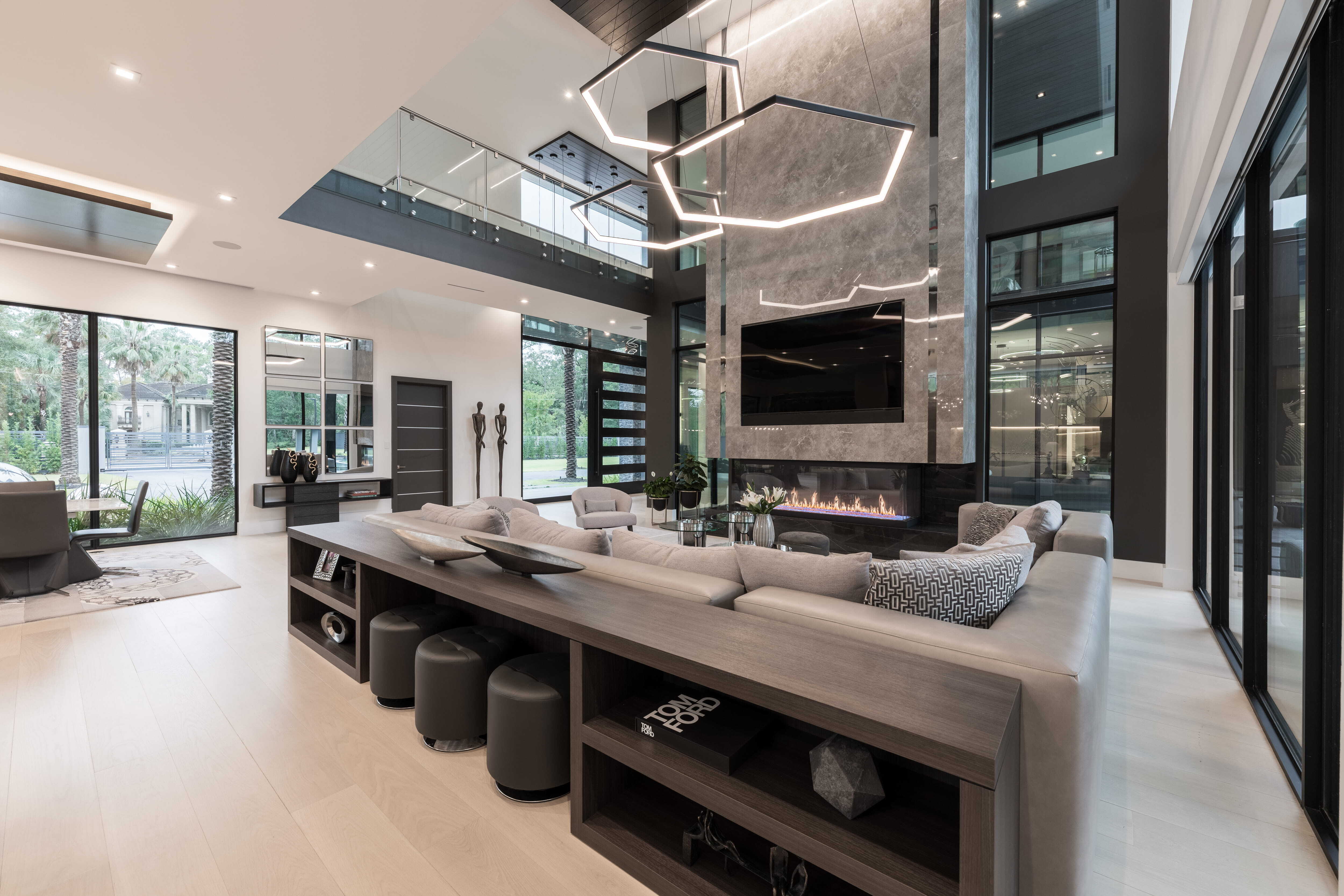 Two-story living room in a modern Memorial Houston custom home featuring a dramatic stone fireplace wall, geometric pendant lighting, expansive glass walls, and open living spaces designed for luxury entertaining.