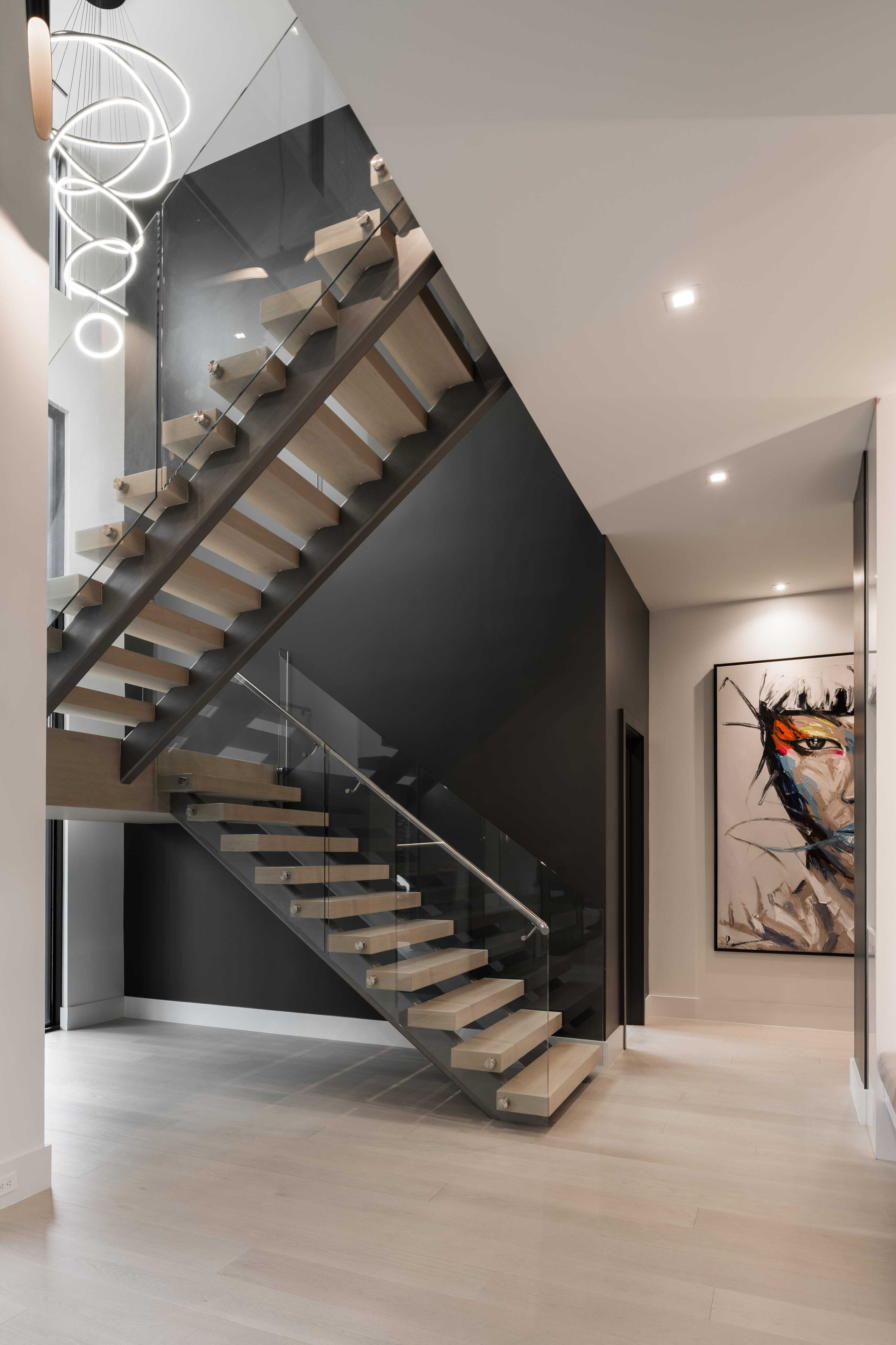 Floating wood staircase with glass railings and sculptural ring chandelier in a dramatic modern entry hall of a luxury custom home in Memorial Houston.