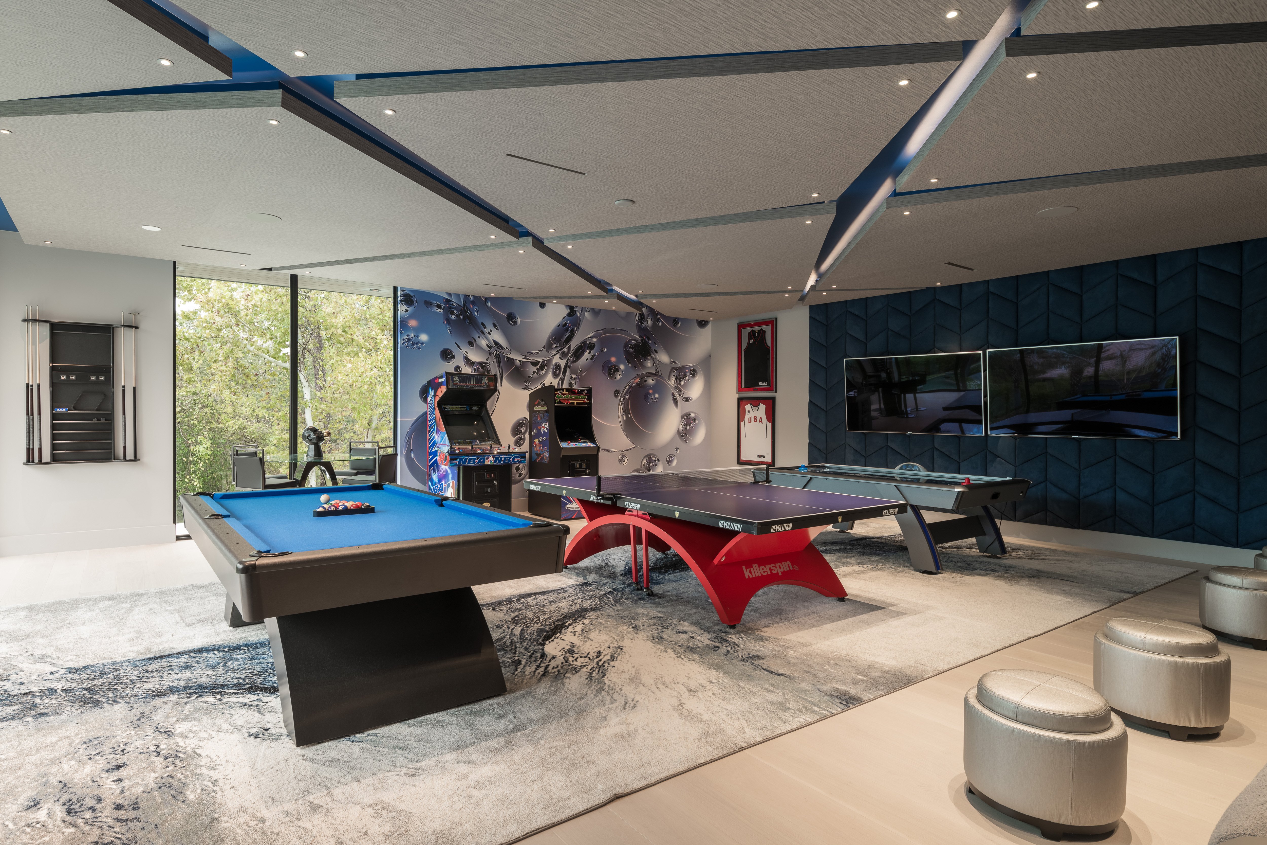 Luxury game room with pool table, ping pong table, arcade machines, and lounge seating, surrounded by floor-to-ceiling windows and contemporary wall finishes inside a modern Memorial Houston custom home.