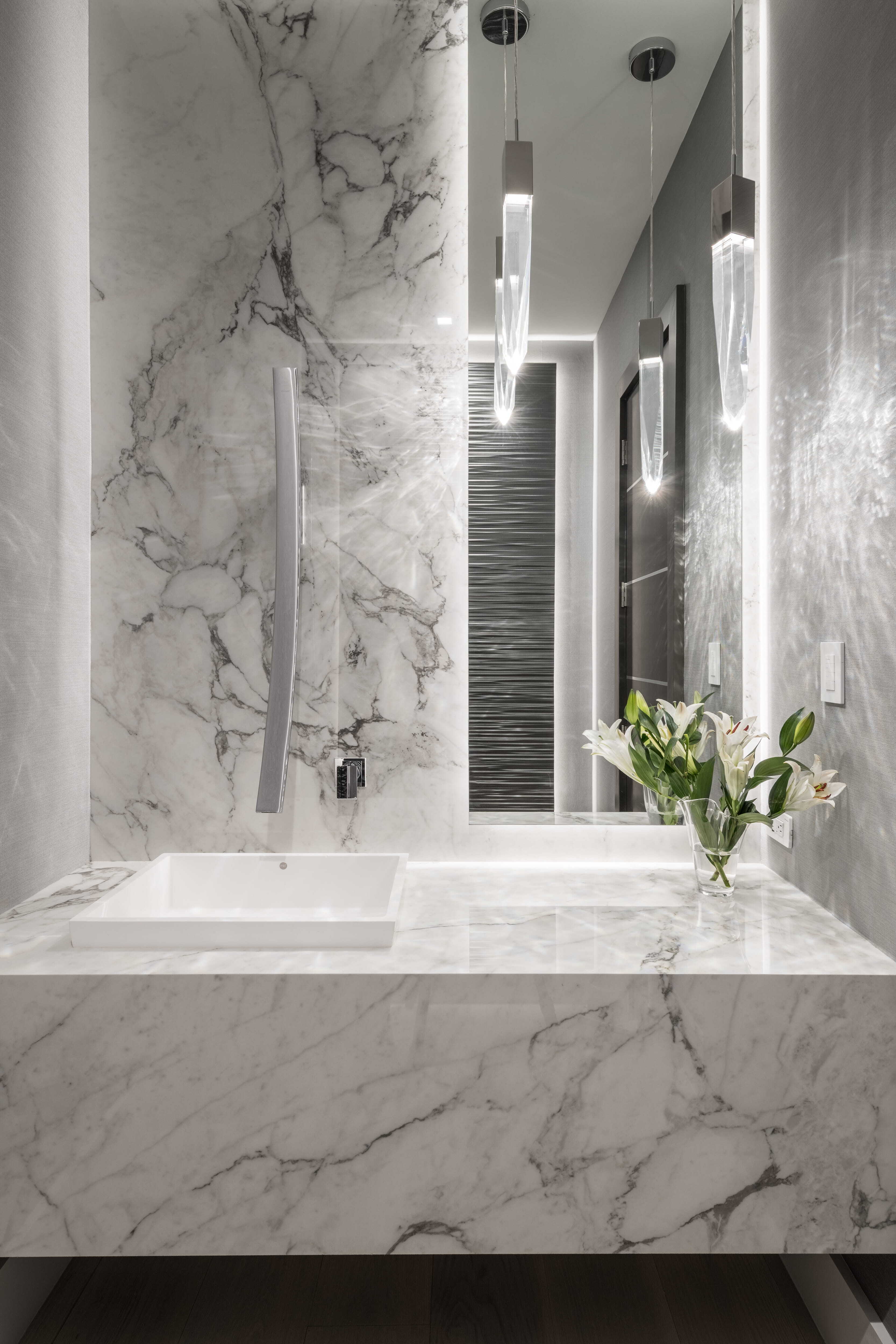 Contemporary powder bath with marble wall and countertop, modern wall-mounted faucet, and crystal pendant lighting creating a refined spa-like space in a luxury Memorial Houston custom home.
