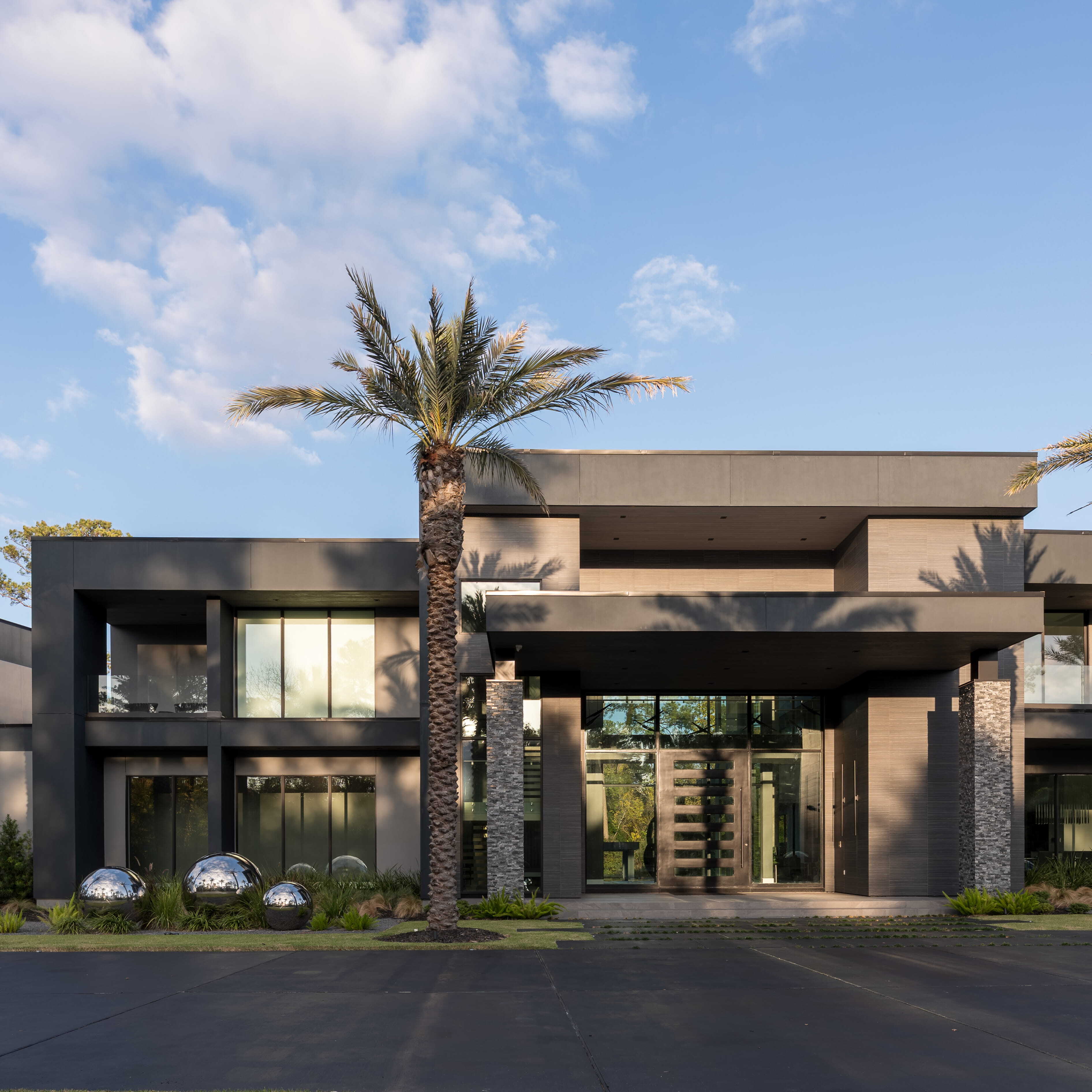 Modern luxury custom home exterior in Memorial Houston featuring clean architectural lines, expansive glass, dramatic overhangs, stone columns, and a large steel pivot front door.