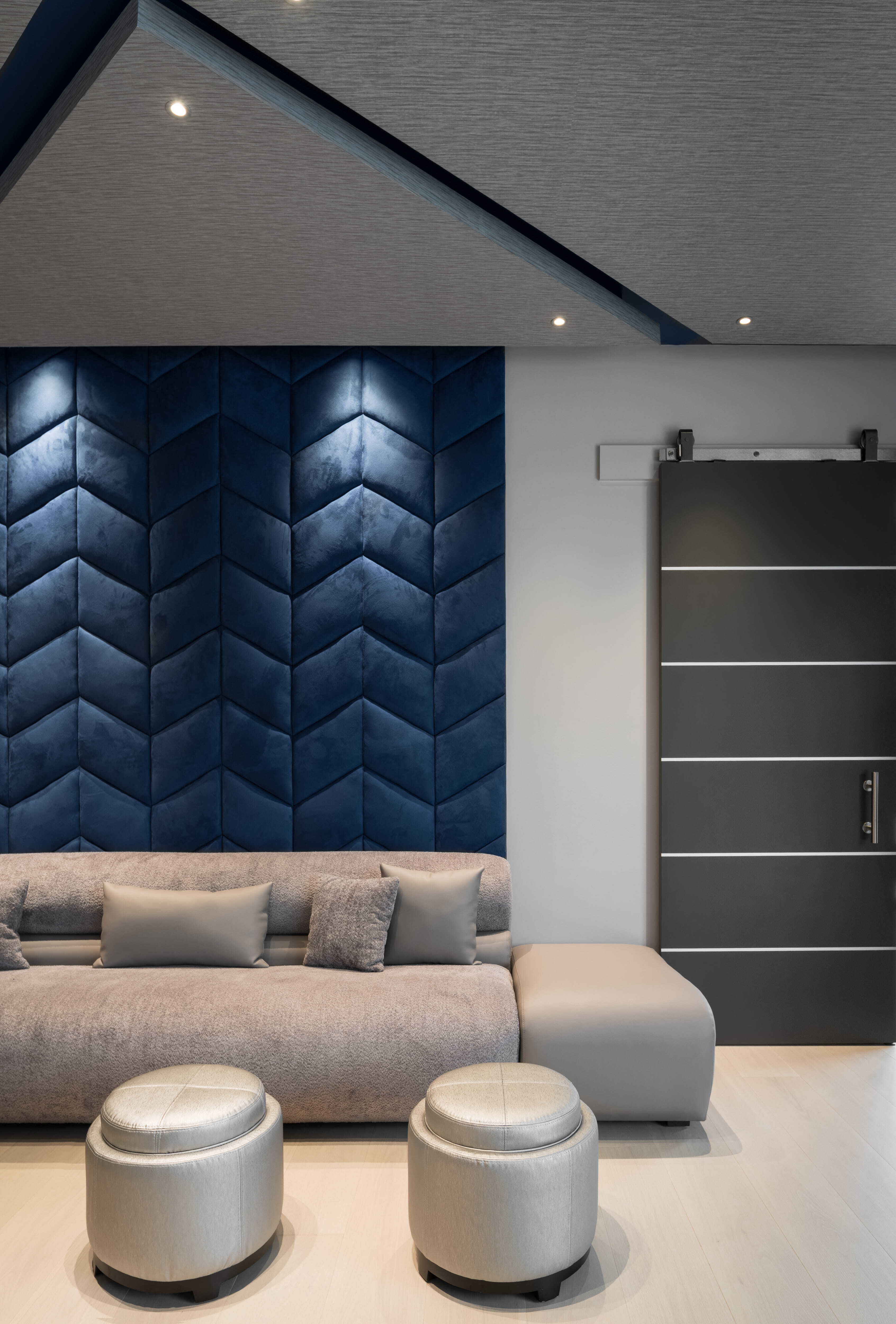 Modern sitting area with sculptural blue upholstered accent wall, neutral sofa seating, round ottomans, and contemporary sliding barn door inside a luxury custom home in Memorial Houston.