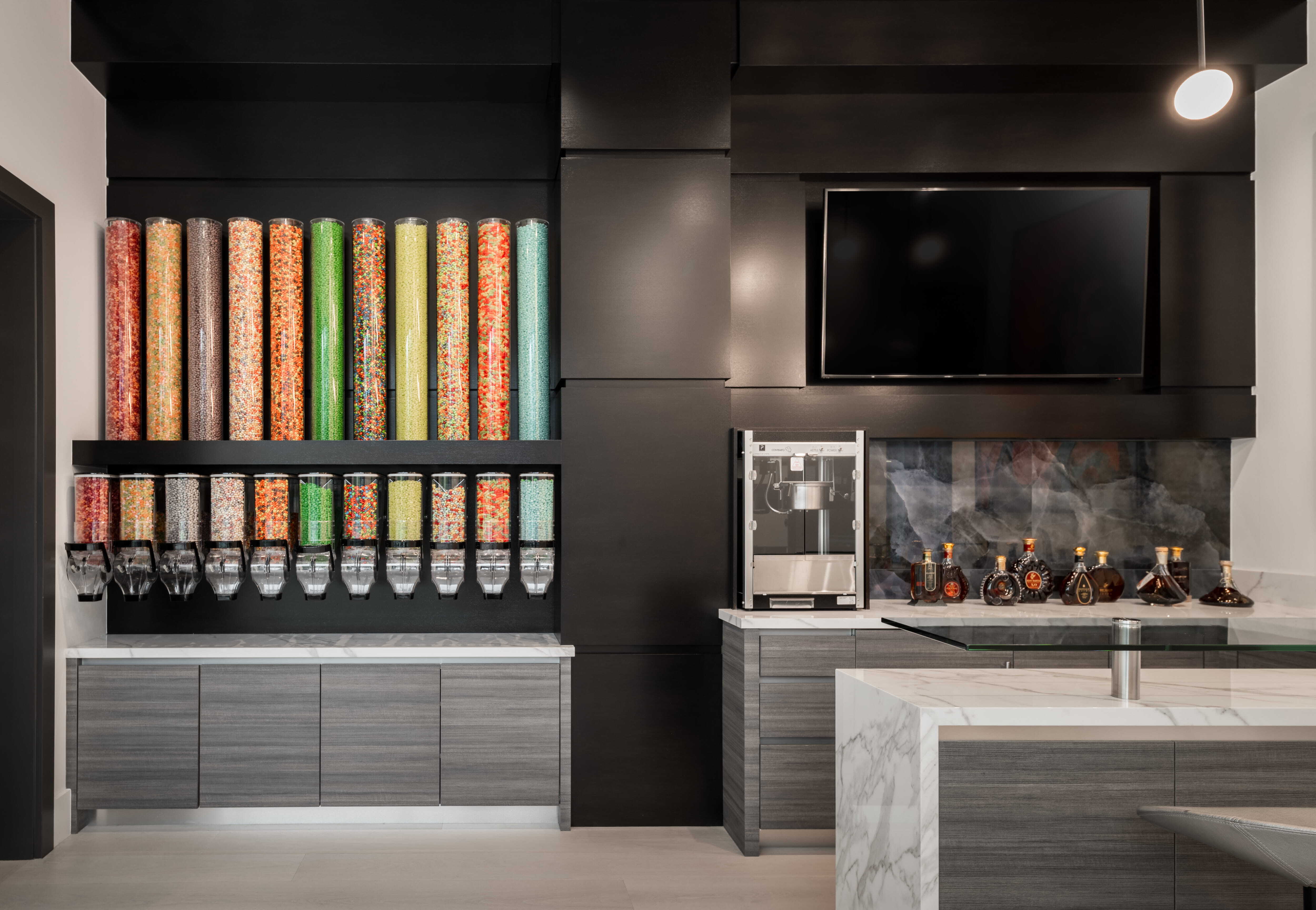 Custom candy bar featuring colorful candy dispensers, marble countertops, modern cabinetry, and built-in entertainment display inside a luxury custom home designed for family gathering and fun.