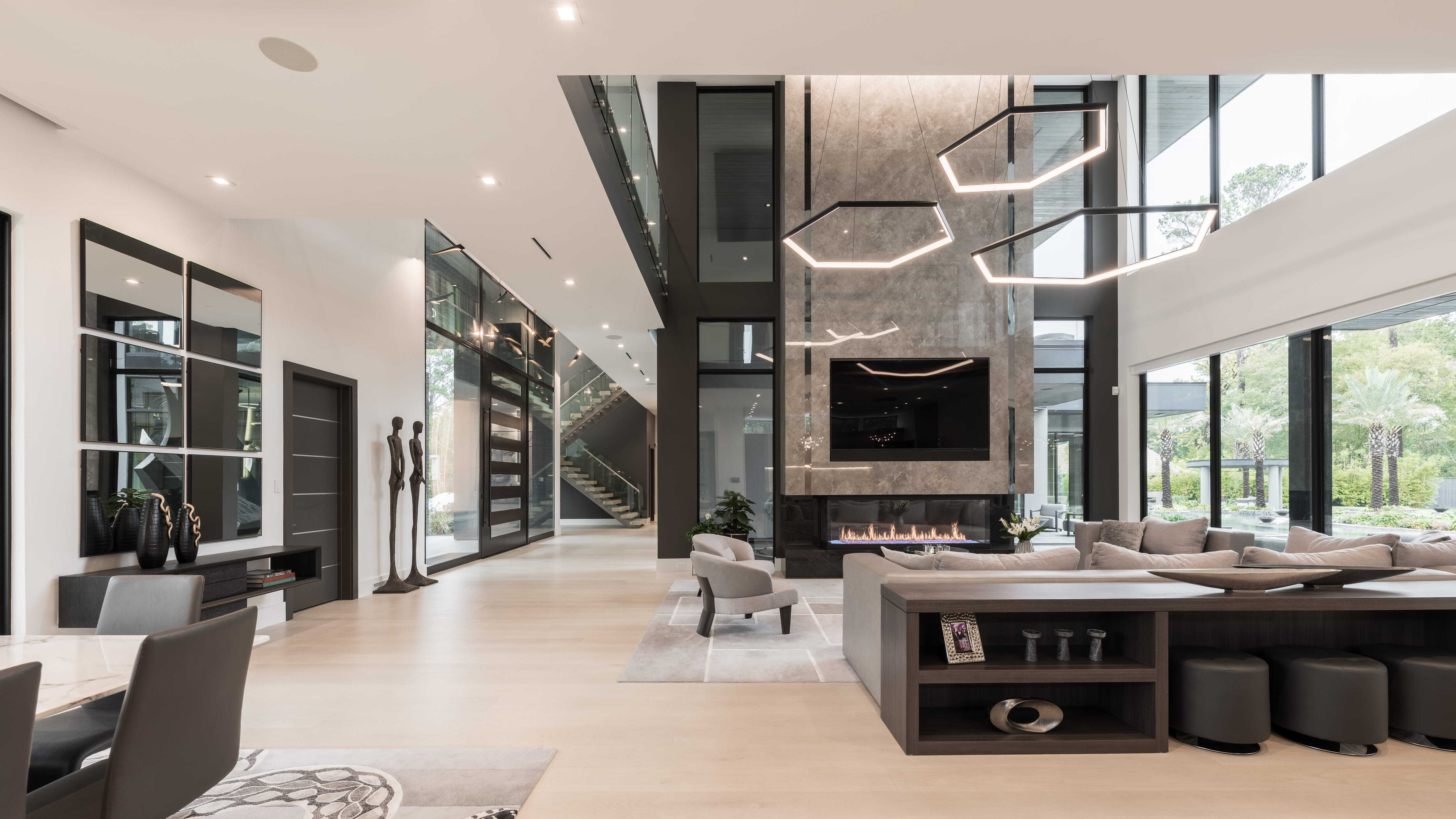 Two-story living room with dramatic stone fireplace wall, sculptural geometric chandelier, floor-to-ceiling glass, and open sightlines to the entry and staircase in a modern luxury custom home in Memorial Houston.