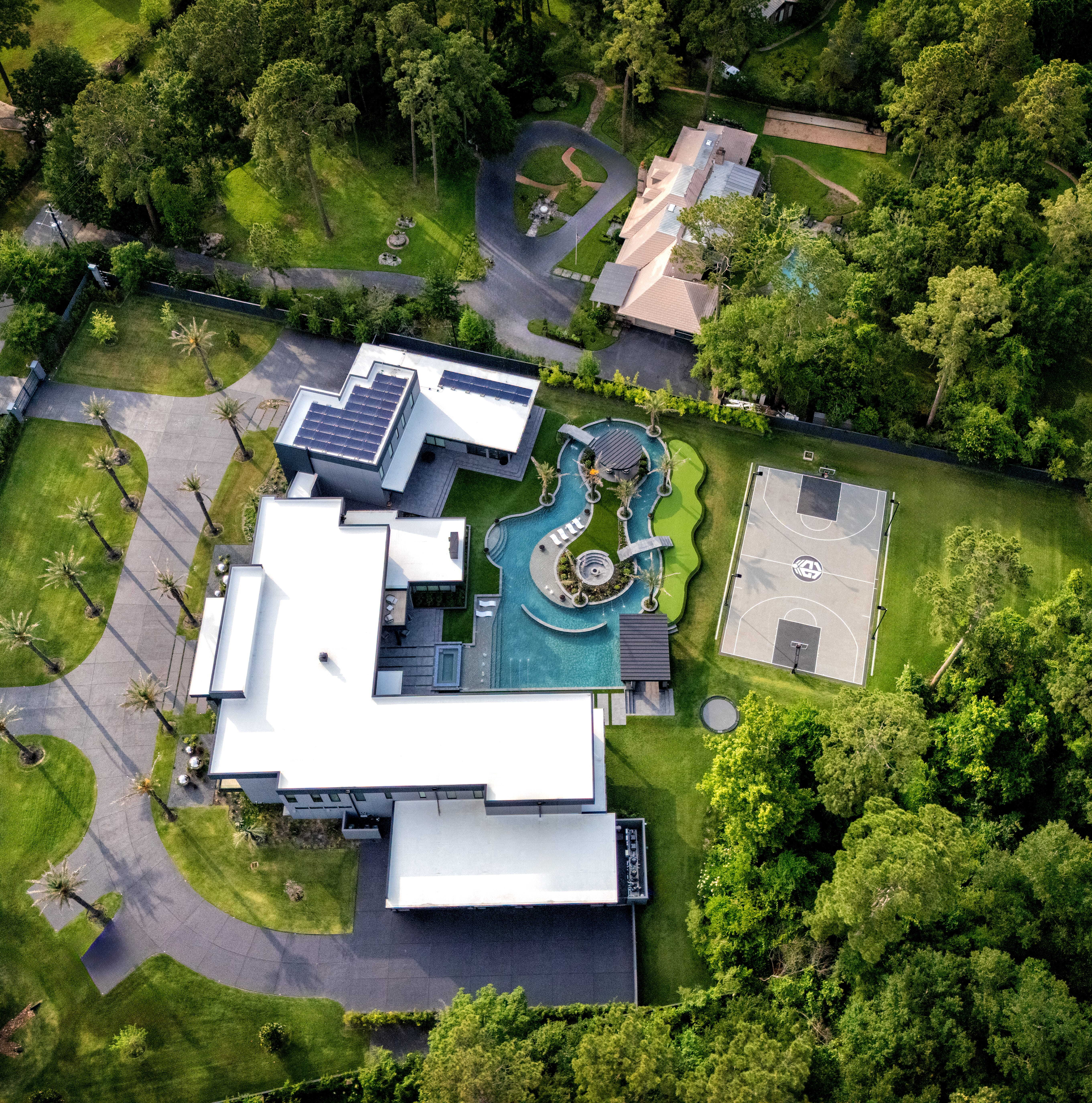 Aerial view of modern luxury estate in Memorial Houston featuring expansive pool with lazy river, swim-up bar, outdoor living areas, basketball court, landscaped grounds, and contemporary architecture.