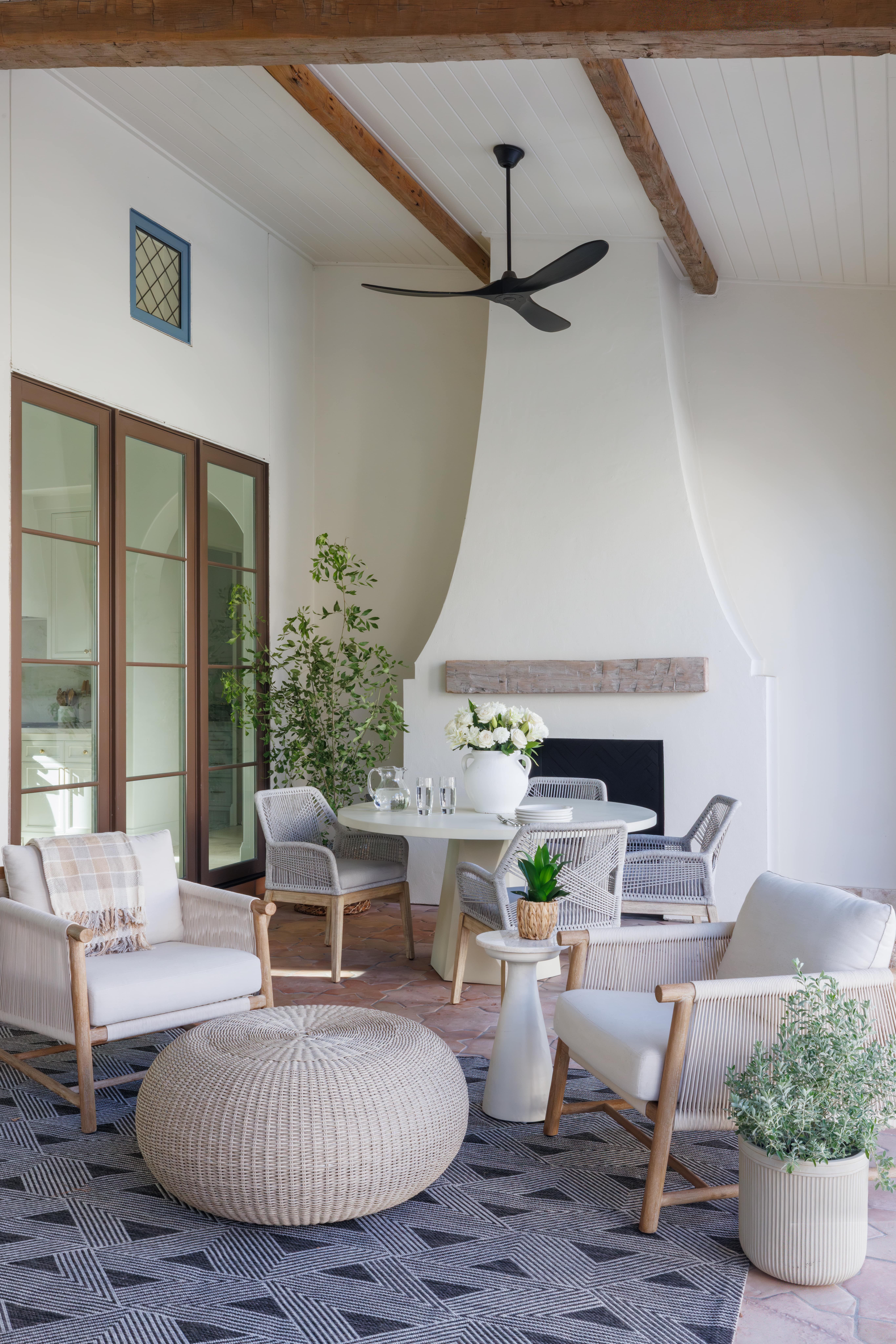 Spanish Hacienda - outdoor terrace seating area with woven lounge chairs, round wicker ottoman, potted plants, and a sculptural stucco fireplace.