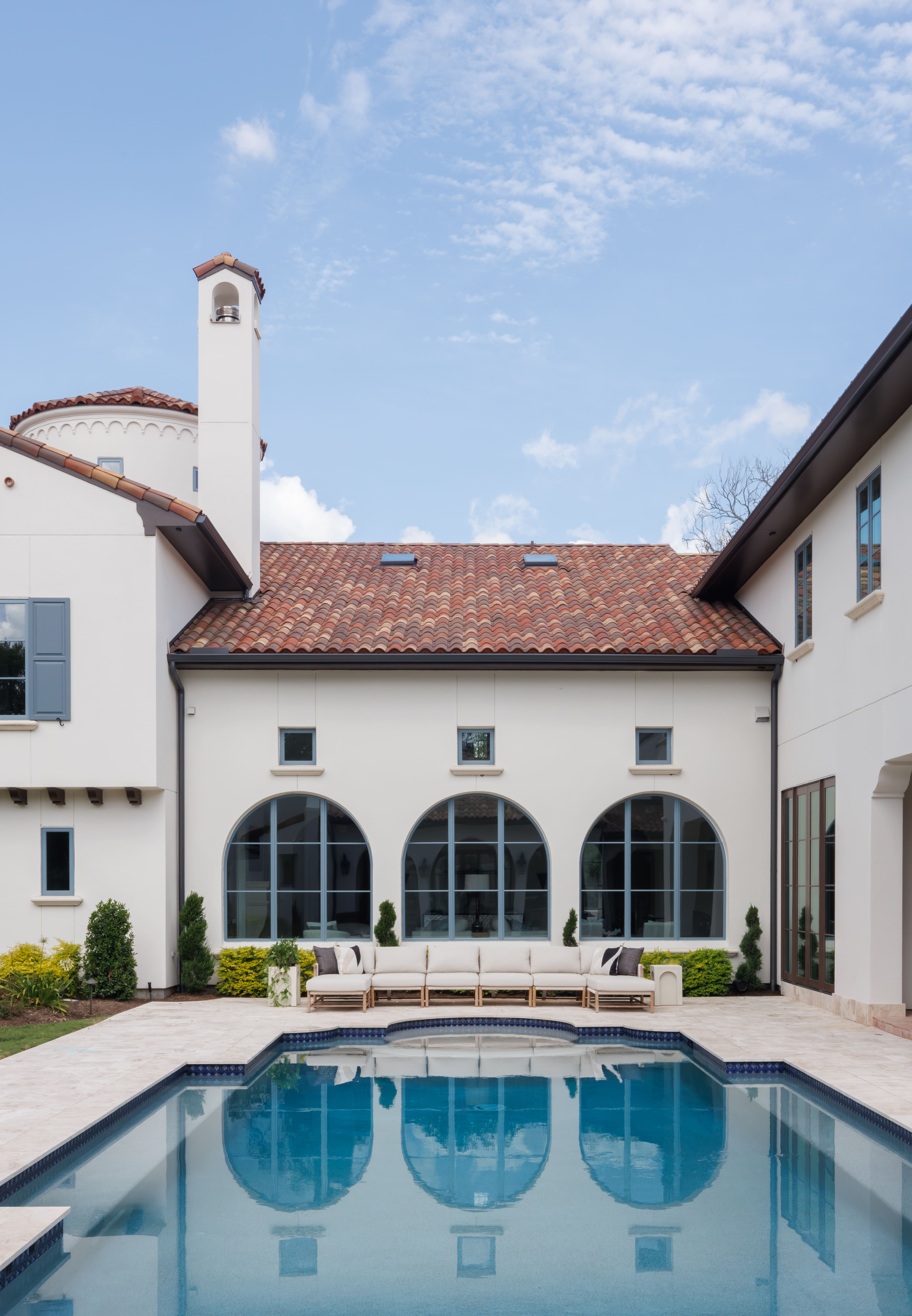 Spanish Hacienda - pool courtyard with arched windows, white stucco façade, terracotta roof tiles, and a long outdoor sofa reflecting in the pool.