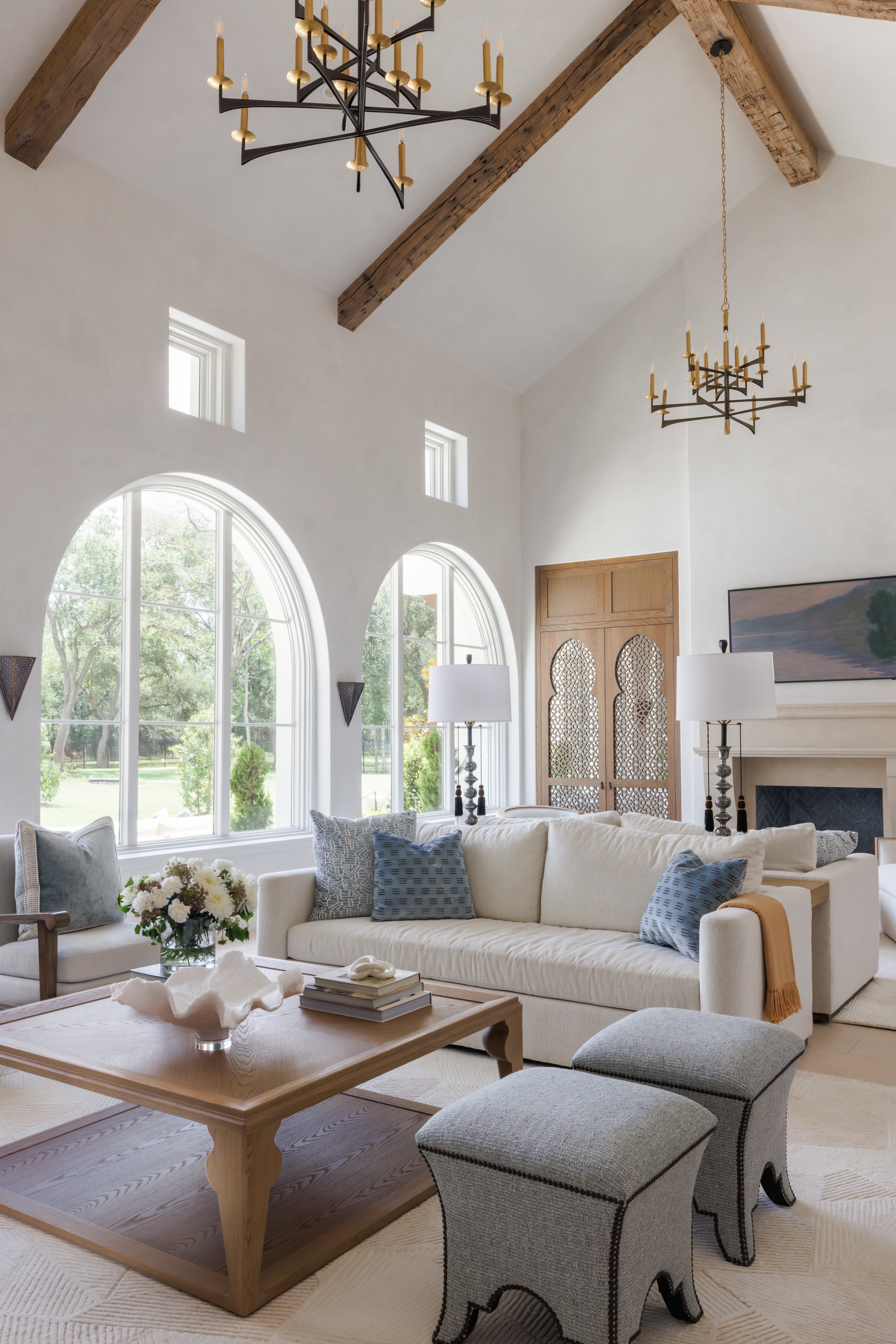 Spanish Hacienda - great room with arched windows, vaulted ceiling, dual iron chandeliers, cream sofas, blue accent pillows, and carved wooden doors with Moorish lattice detail.