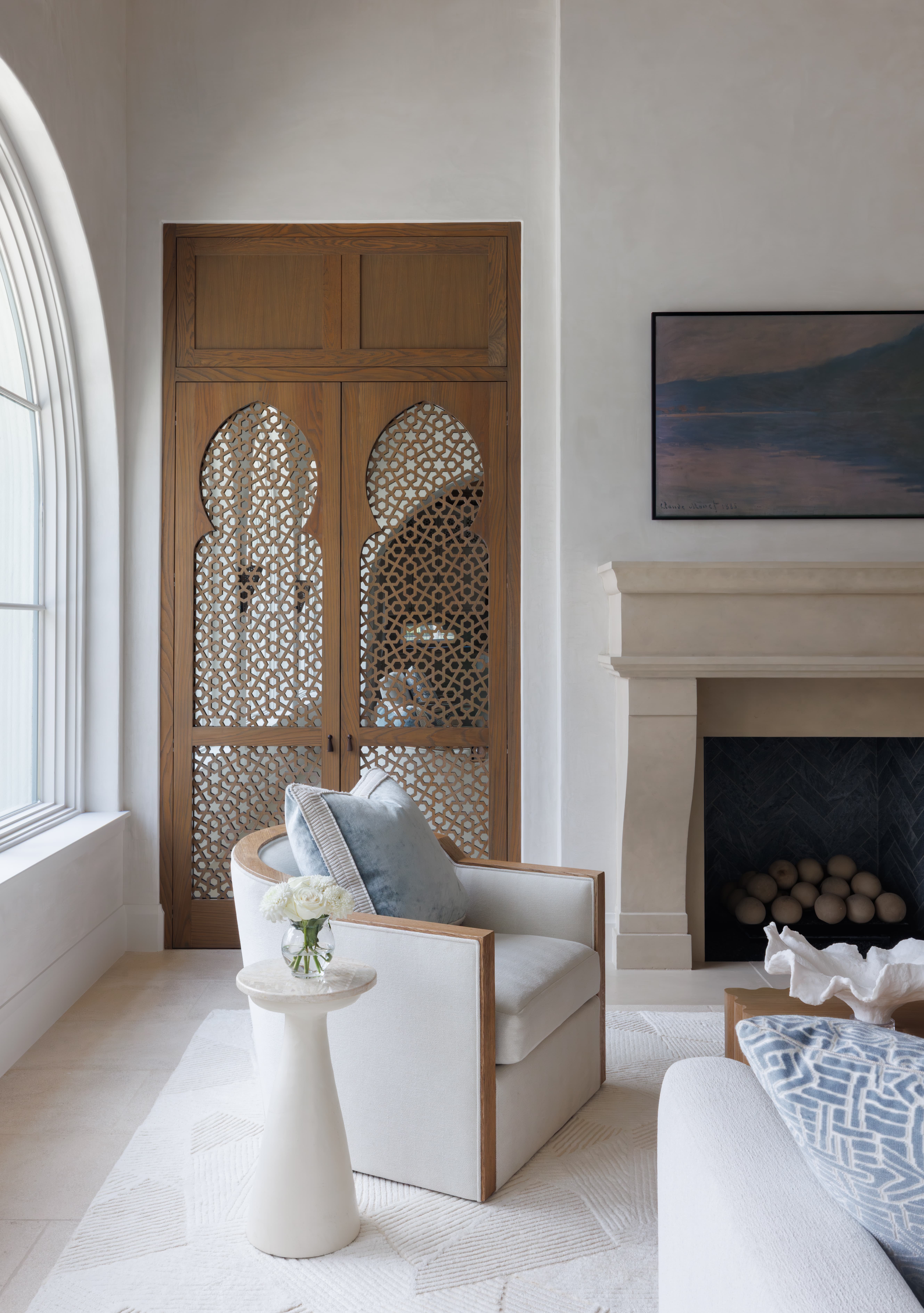Spanish Hacienda - living room seating vignette with cream lounge chair, marble side table, sculpted stone fireplace, and carved Moorish-inspired wooden cabinet doors.