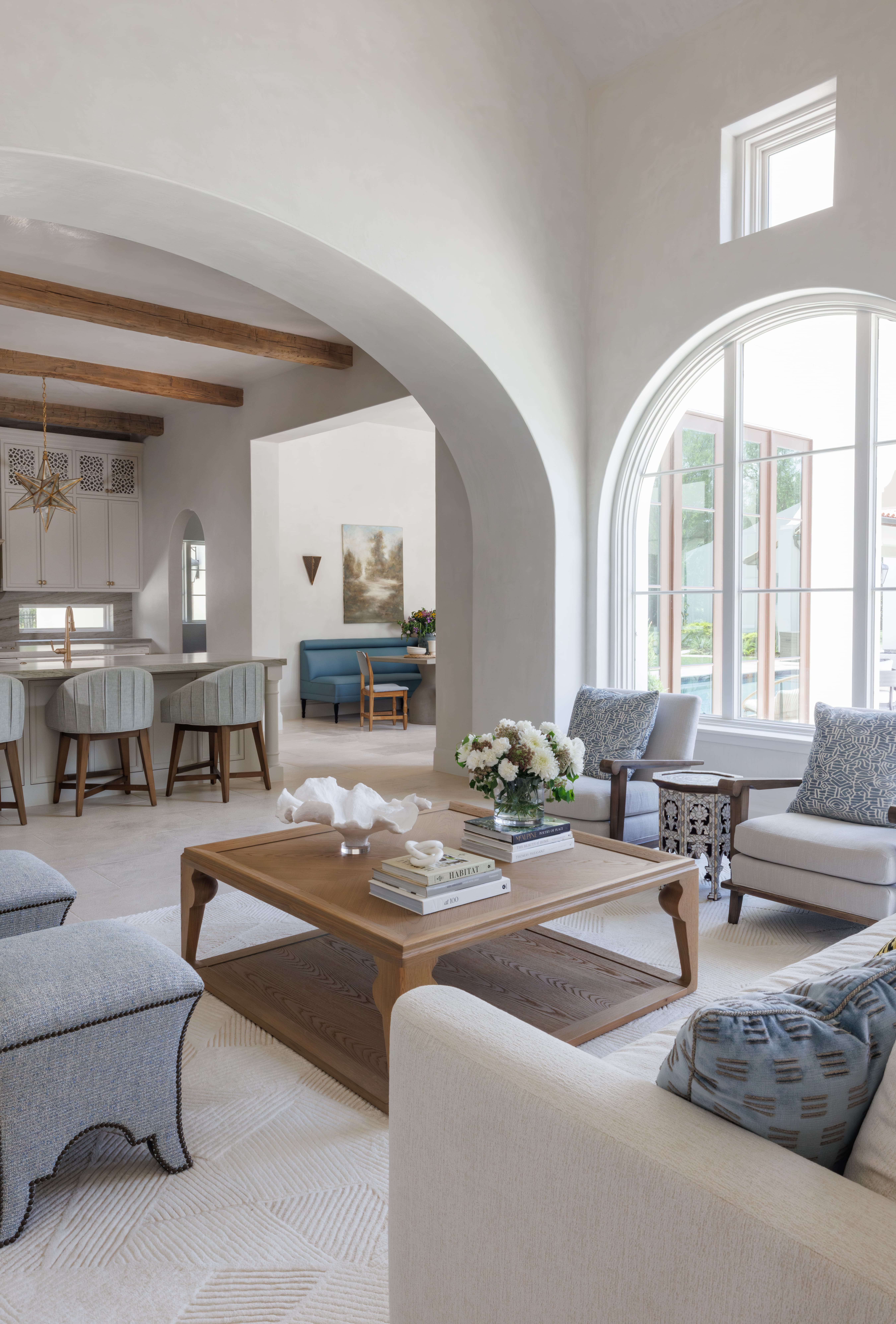 Spanish Hacienda - open-concept view from the living room into the kitchen and breakfast nook, showcasing arched openings, soft plaster walls, exposed beams, and layered natural textures.