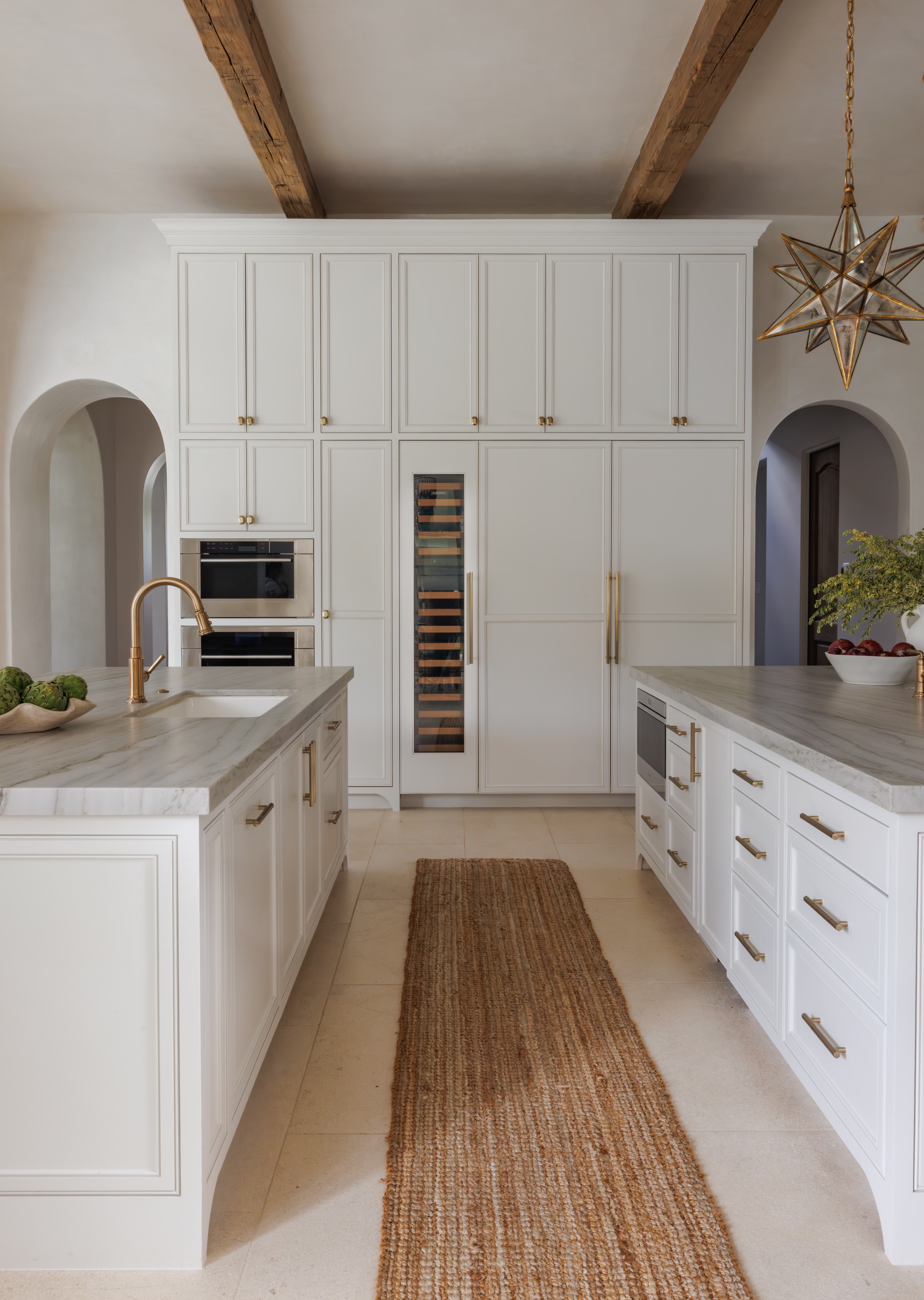 Spanish Hacienda - kitchen with dual islands, integrated paneled appliances, wine storage column, brass hardware, and warm wood ceiling beams for a refined, soft-white palette.