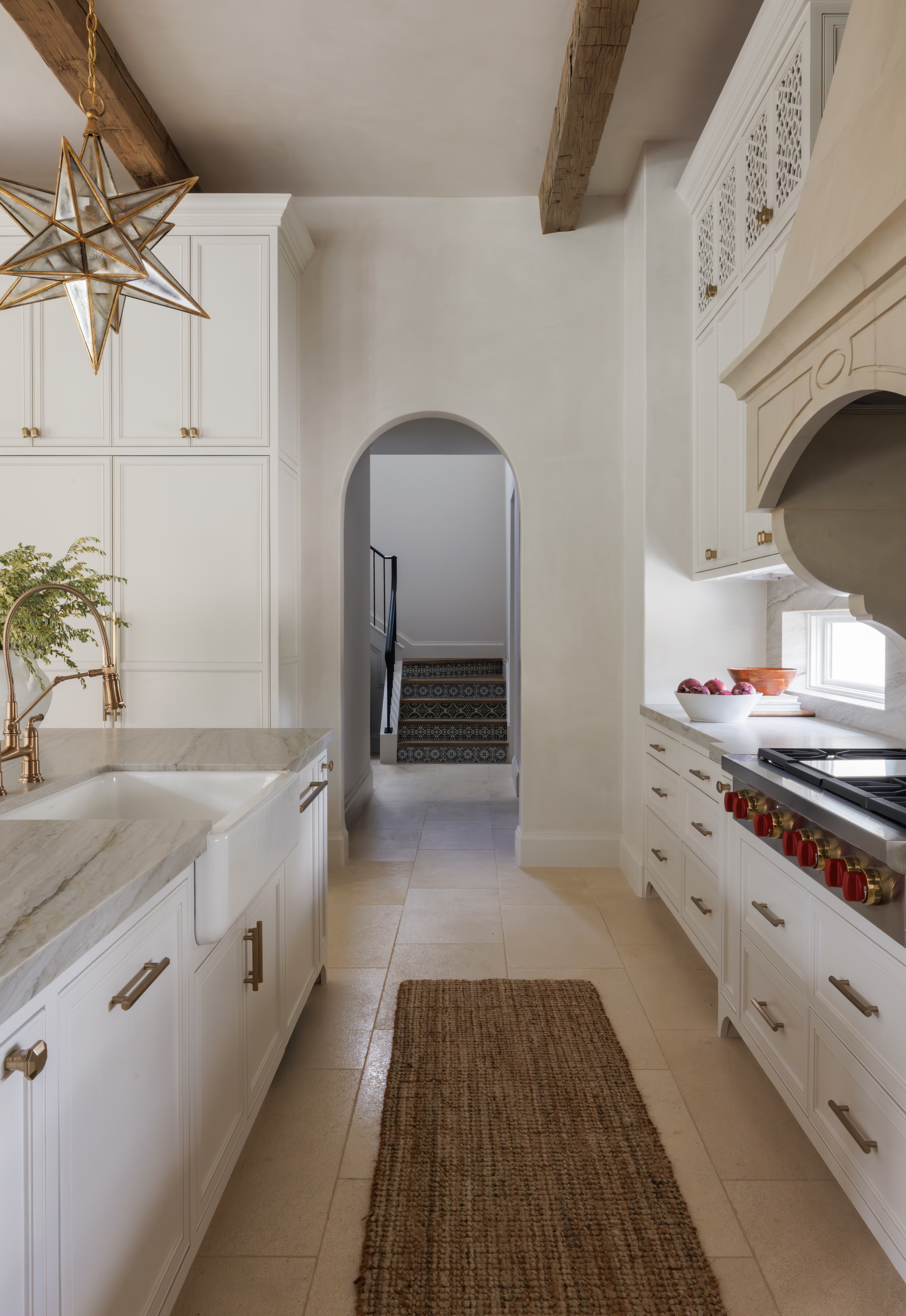 Spanish Hacienda - kitchen hallway with arched doorway leading to a tile-accented staircase, featuring marble countertops, brass fixtures, and a lantern-style star pendant.