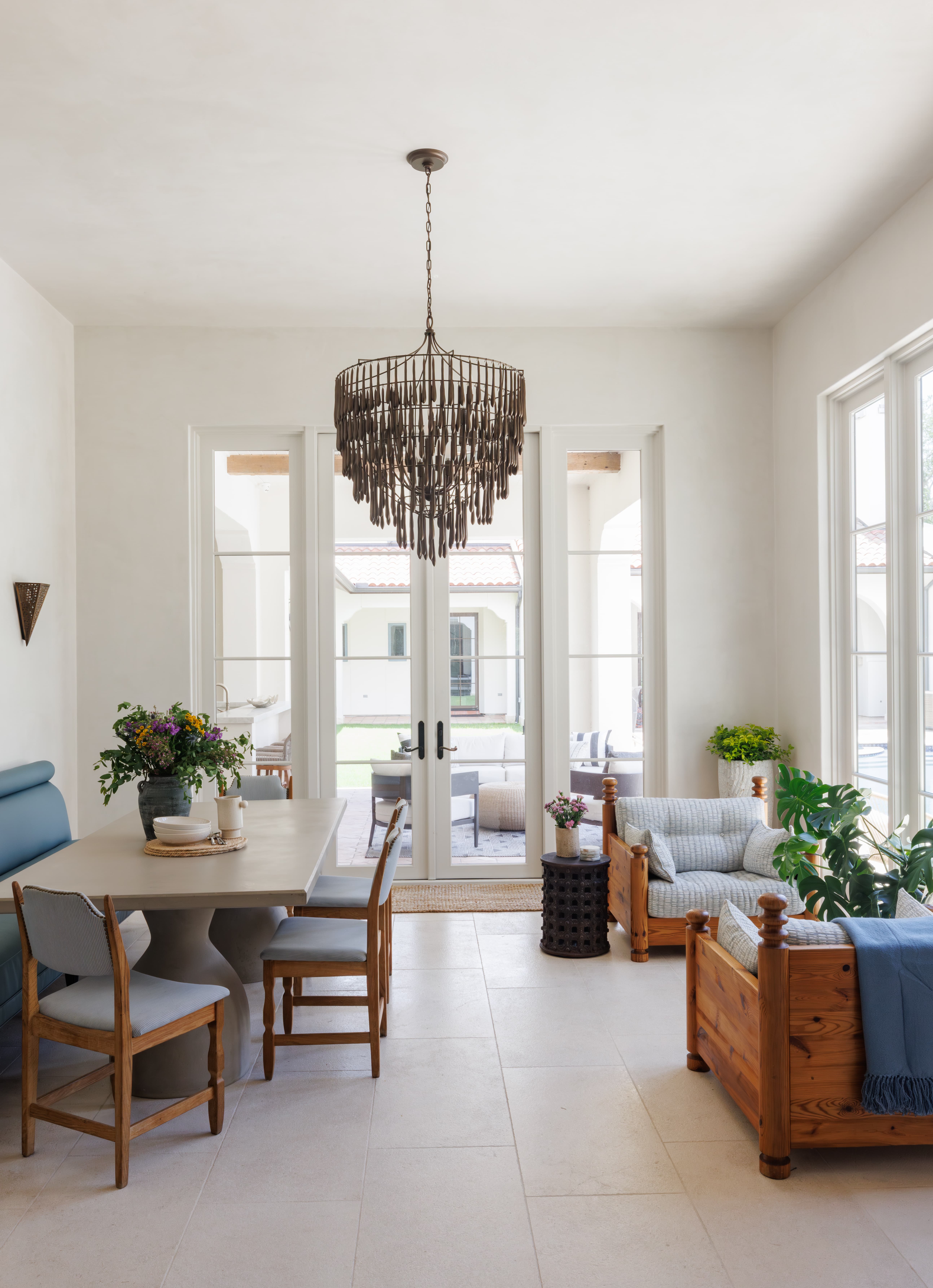 Spanish Hacienda - sunroom with tall windows, wood-framed lounge chairs, blue textiles, indoor greenery, and French doors that frame views of the courtyard patio.