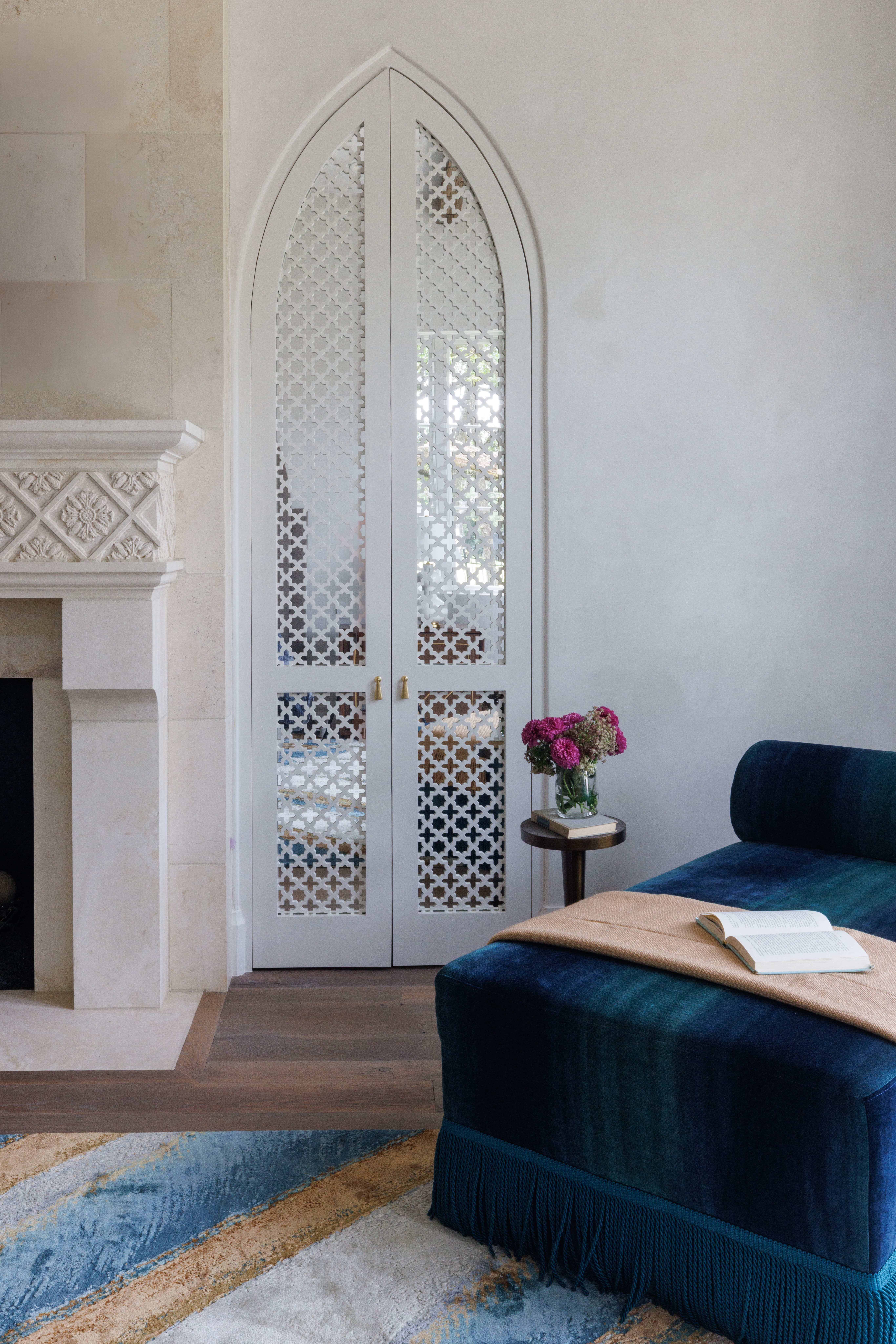 Spanish Hacienda – Bedroom sitting area featuring arched patterned cabinet doors, stone fireplace surround, velvet chaise lounge, and soft layered textiles.