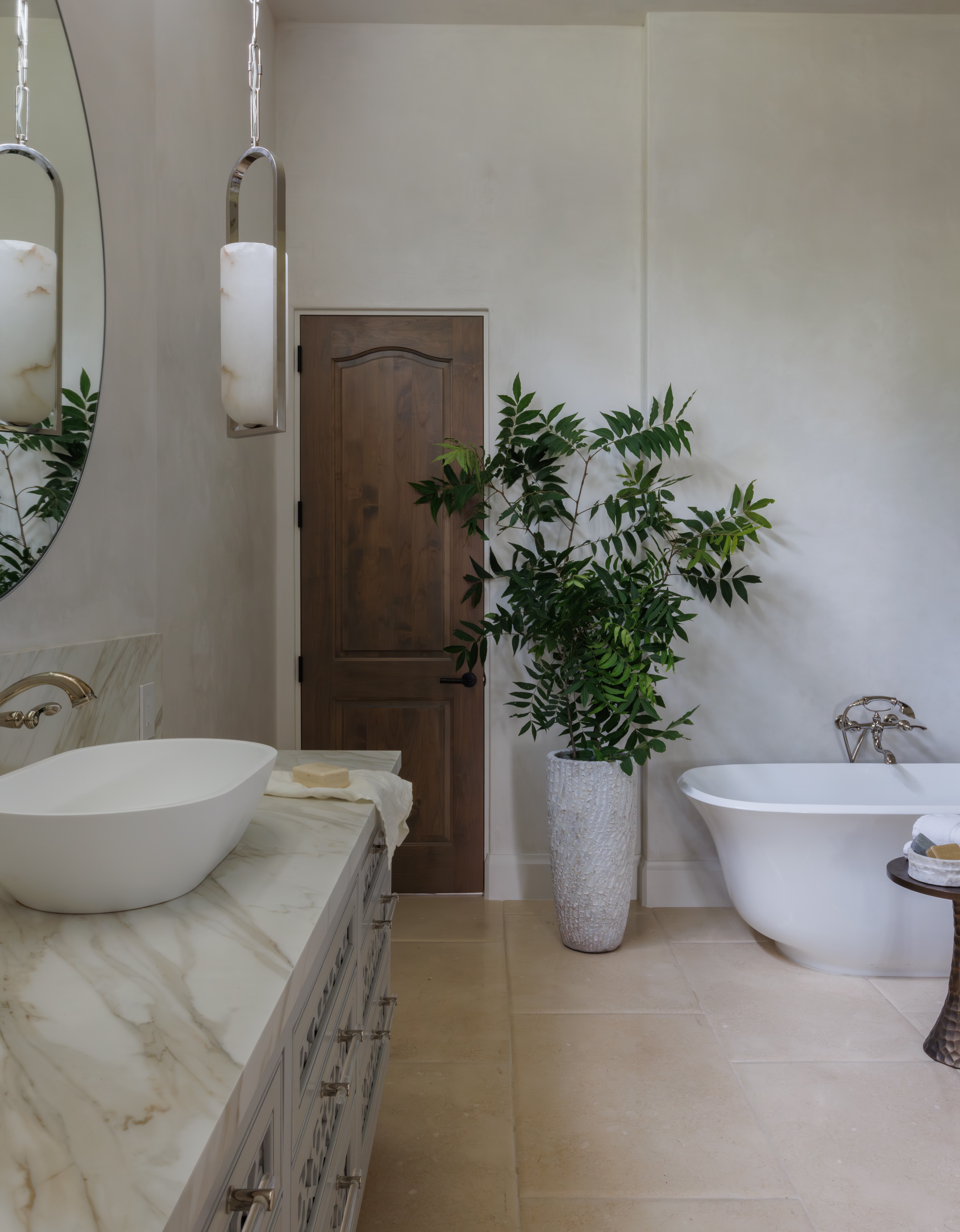 Spanish Hacienda – Bathroom vignette with marble-top vanity, vessel sink, warm wood door, large ceramic planter, and sculptural freestanding tub.