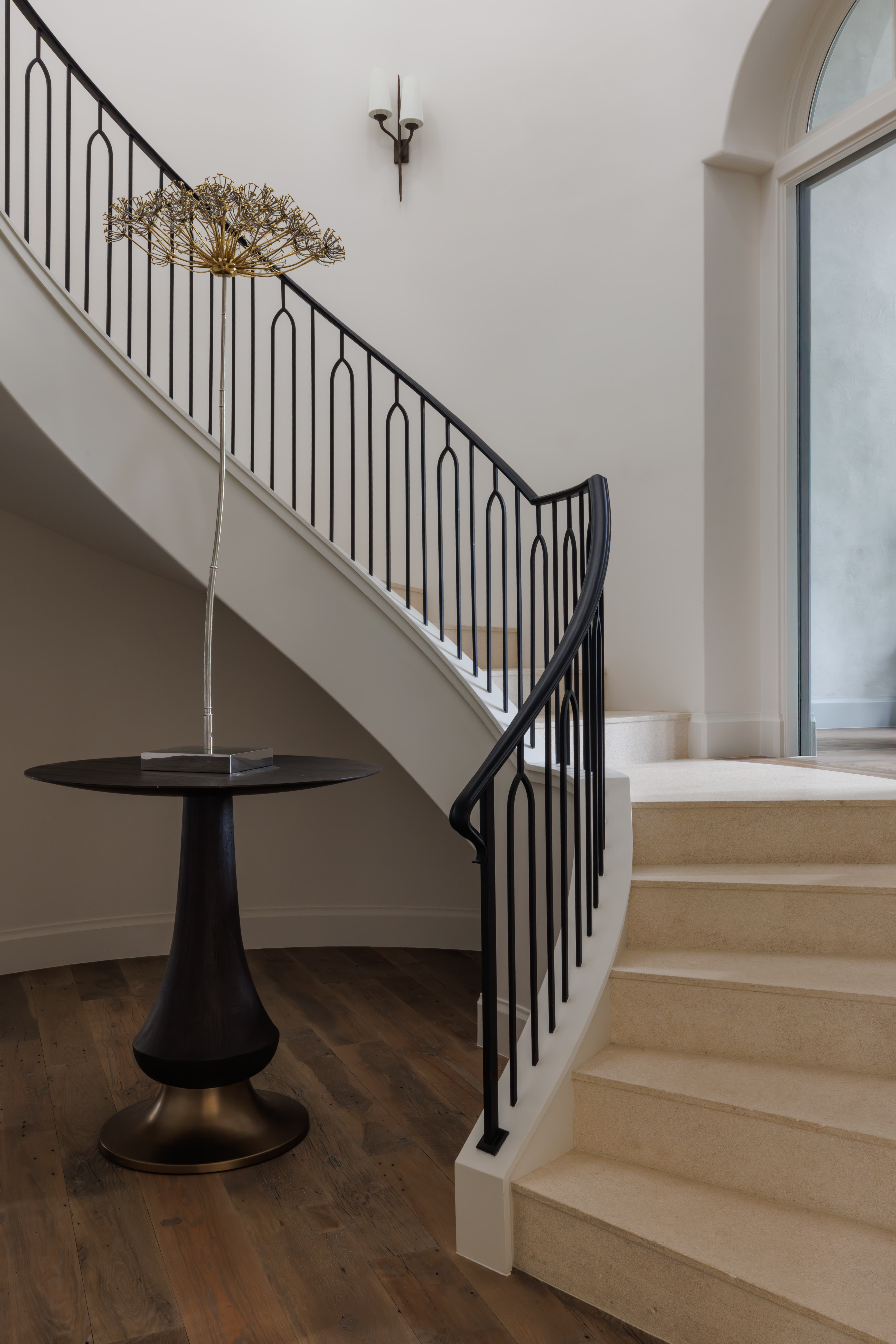 Spanish Hacienda – Curved stone staircase with custom iron railing, round pedestal table, arched window, and soft natural light.