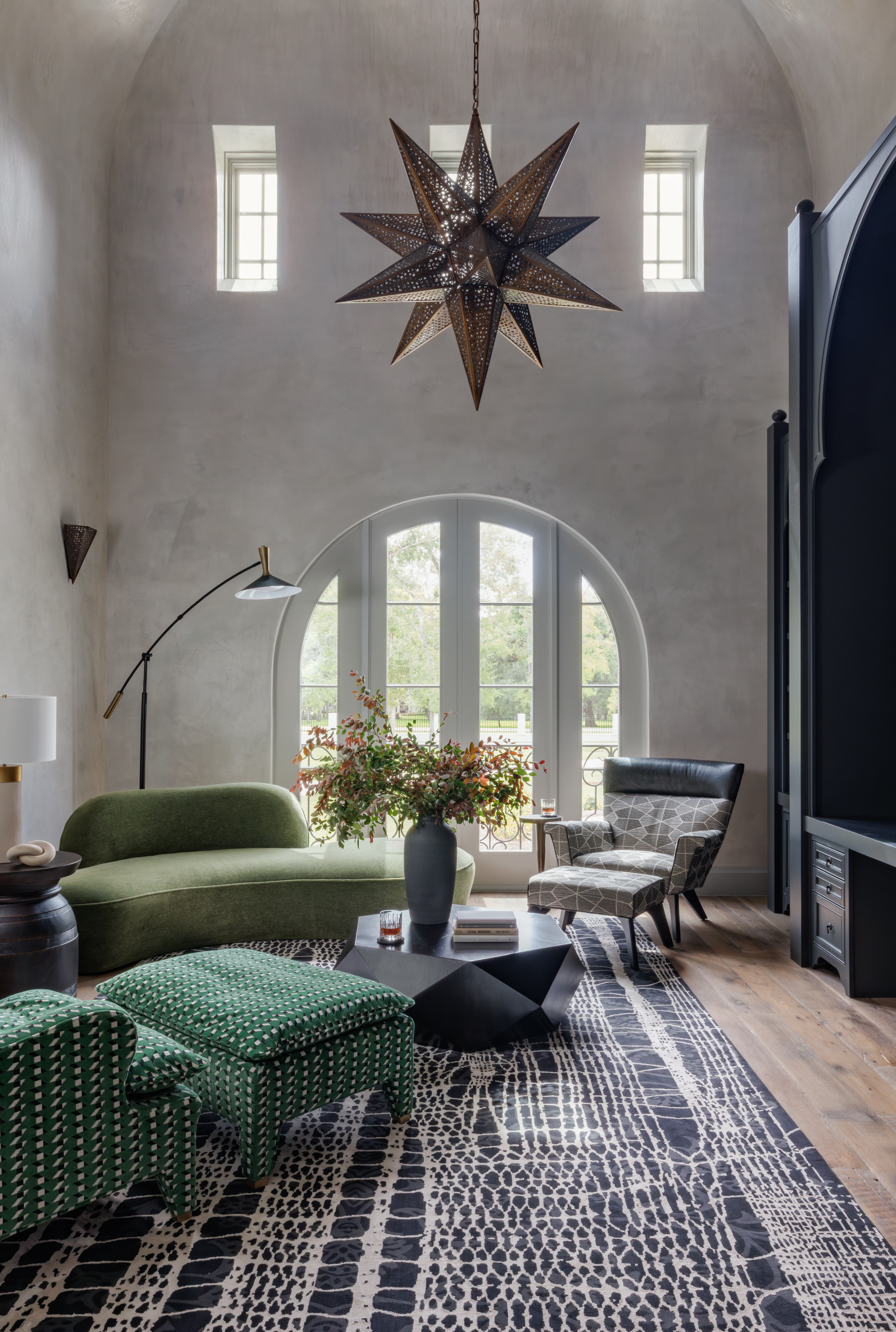 Spanish Hacienda – Vaulted living room with a pierced metal star chandelier, arched French doors, layered modern seating, sculptural coffee table, and patterned area rug.