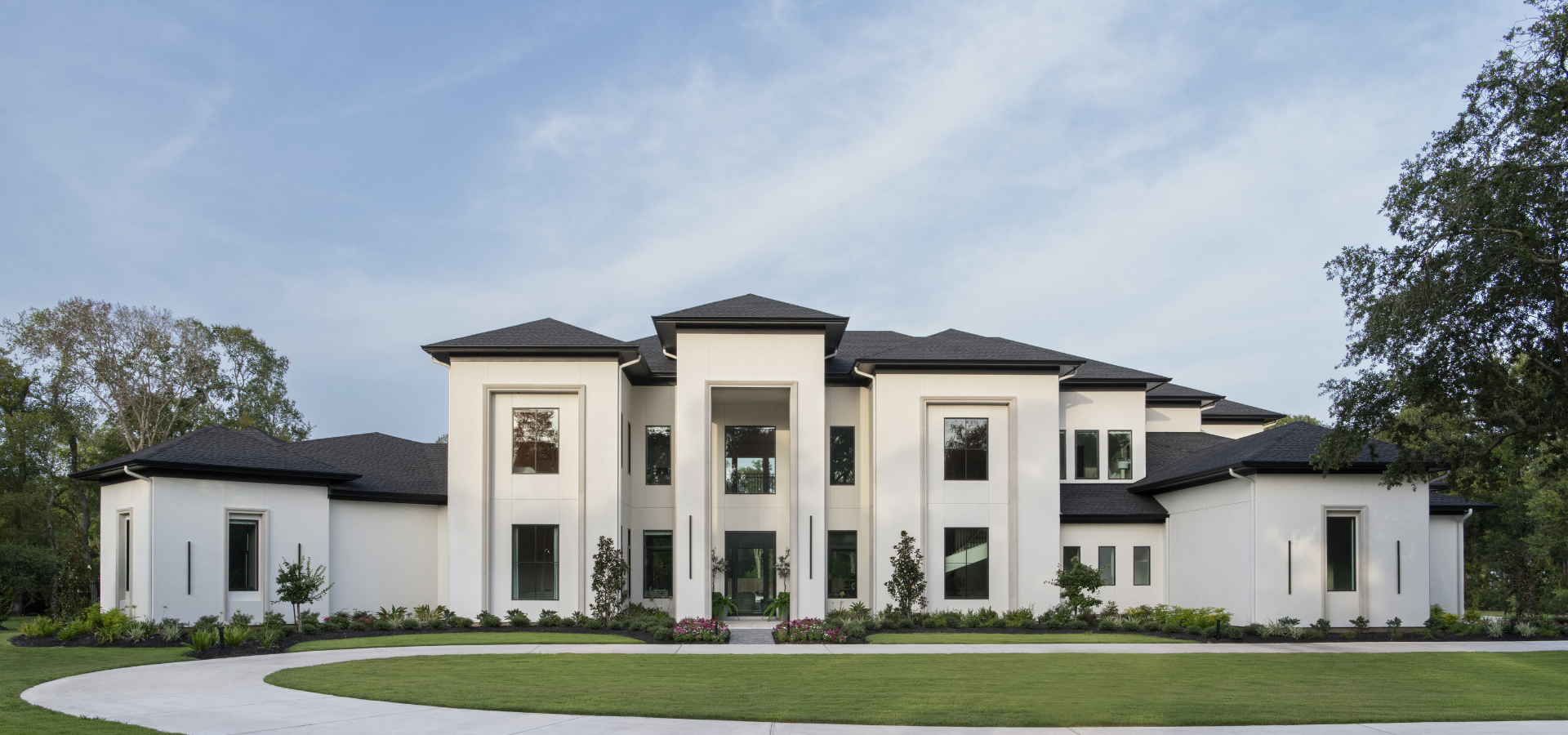 Front elevation of the Transitional Estate featuring a white façade, dark rooflines, large windows, and a circular driveway. Front elevation of the Transitional Estate featuring a white façade, dark rooflines, large windows, and a circular driveway.