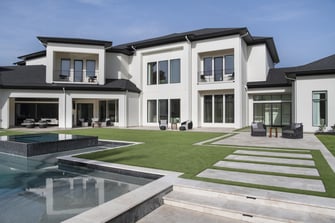 Backyard view of the estate with expansive windows, covered patios, seating areas, and a modern pool design.