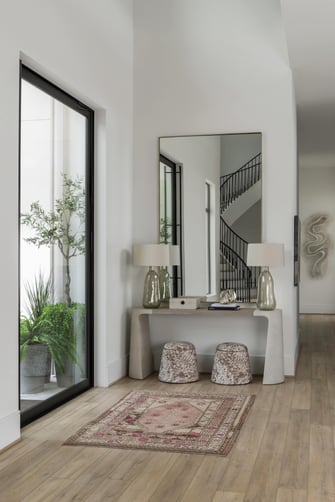 Entry hall with modern console table, oversized mirror, decorative stools, and view of a curved staircase.