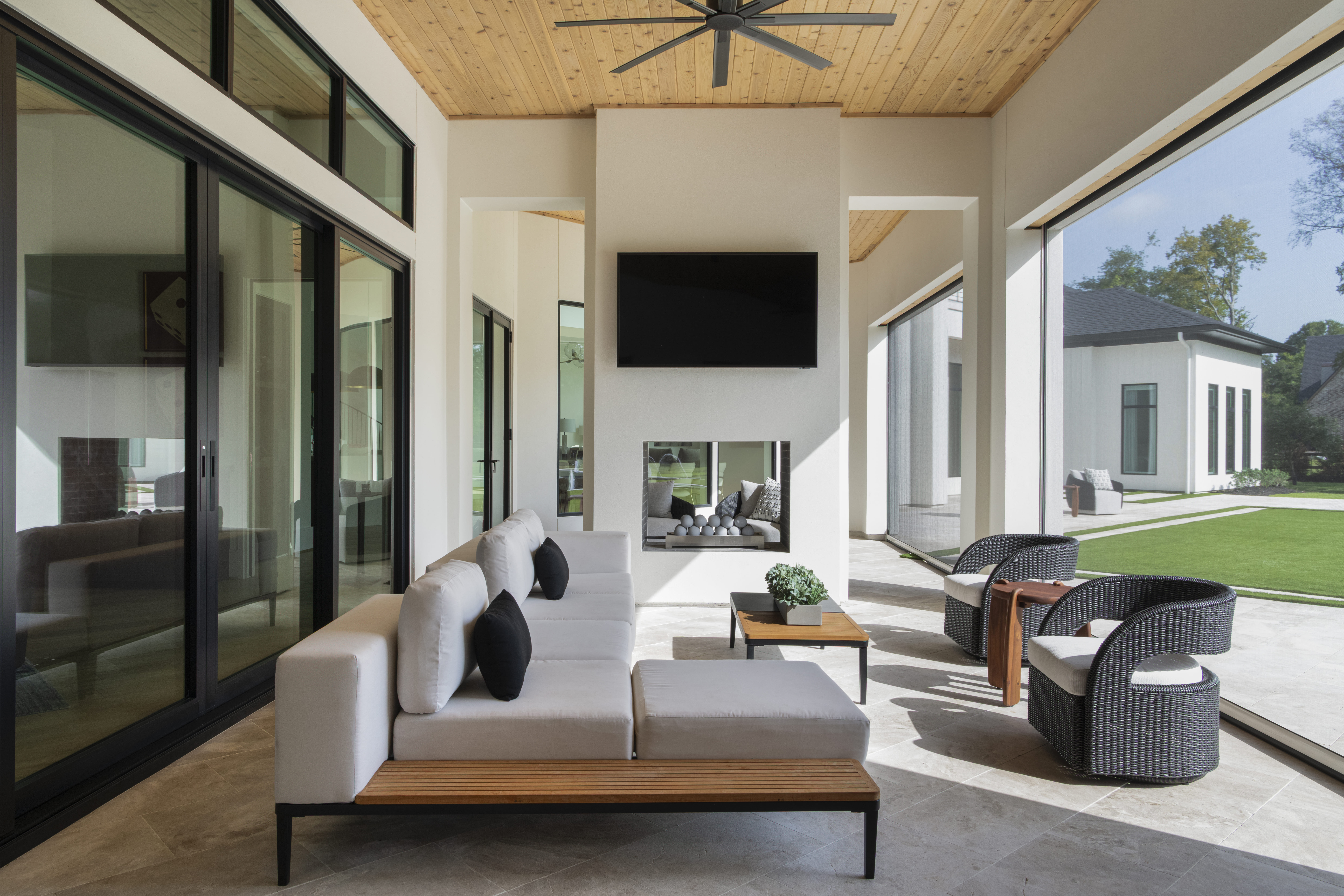 Outdoor lounge with cushioned seating, a ceiling fan, and open views of the landscaped backyard and adjacent structures.