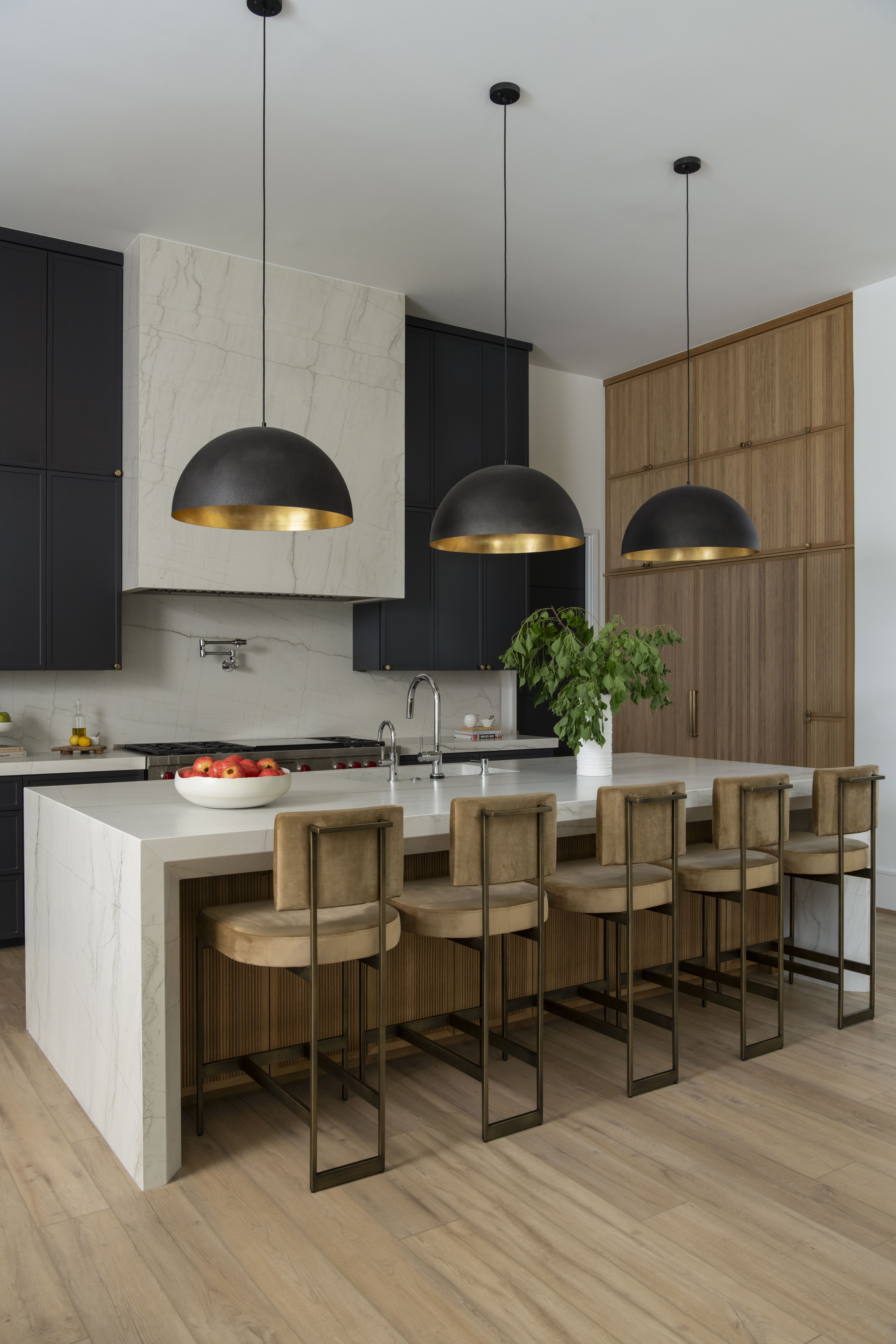 Contemporary kitchen featuring a marble waterfall island, brass-lined pendant lights, wood cabinetry, and suede barstools.