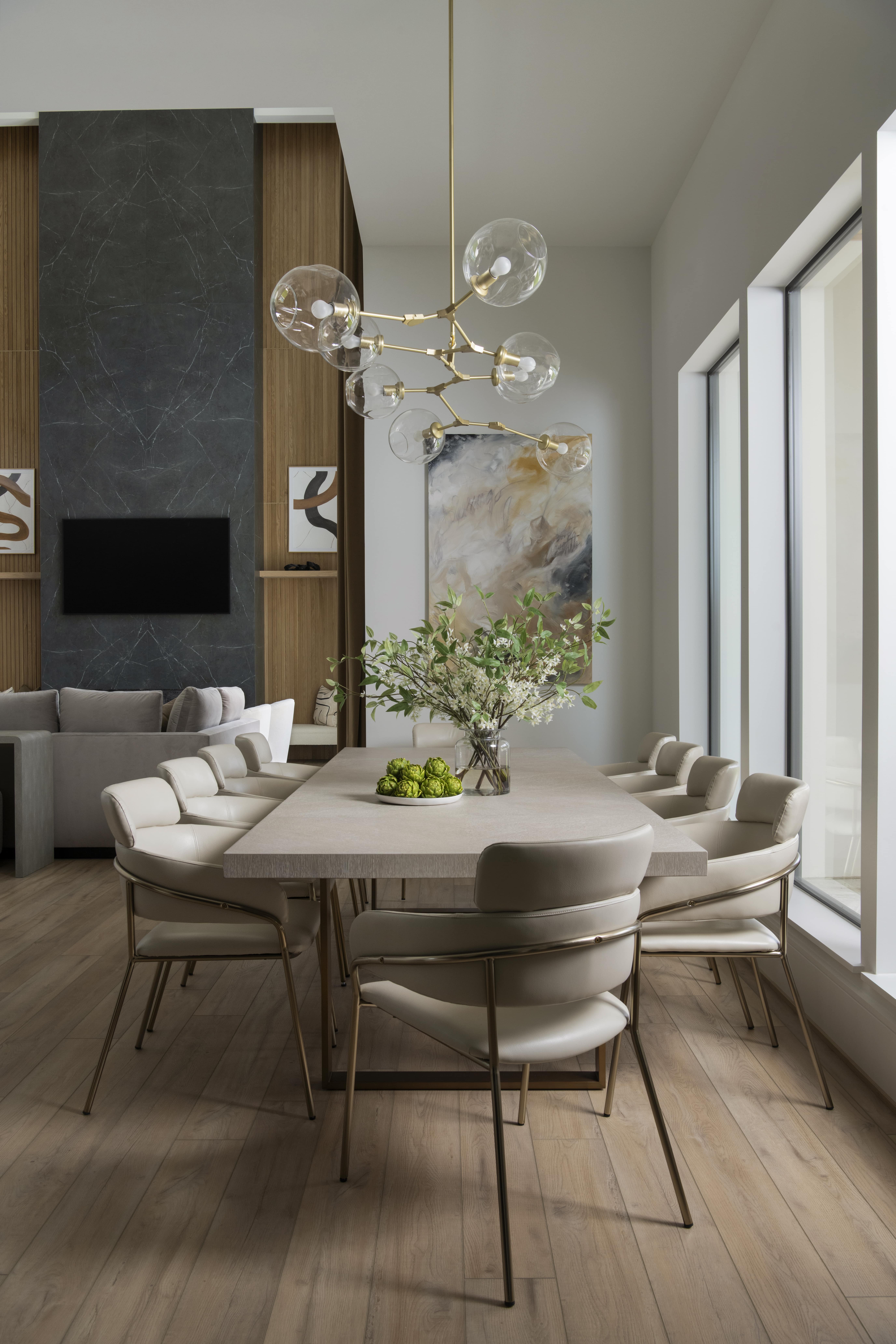 Dining area beside a dark stone fireplace wall, featuring neutral seating and a modern brass-and-glass chandelier.