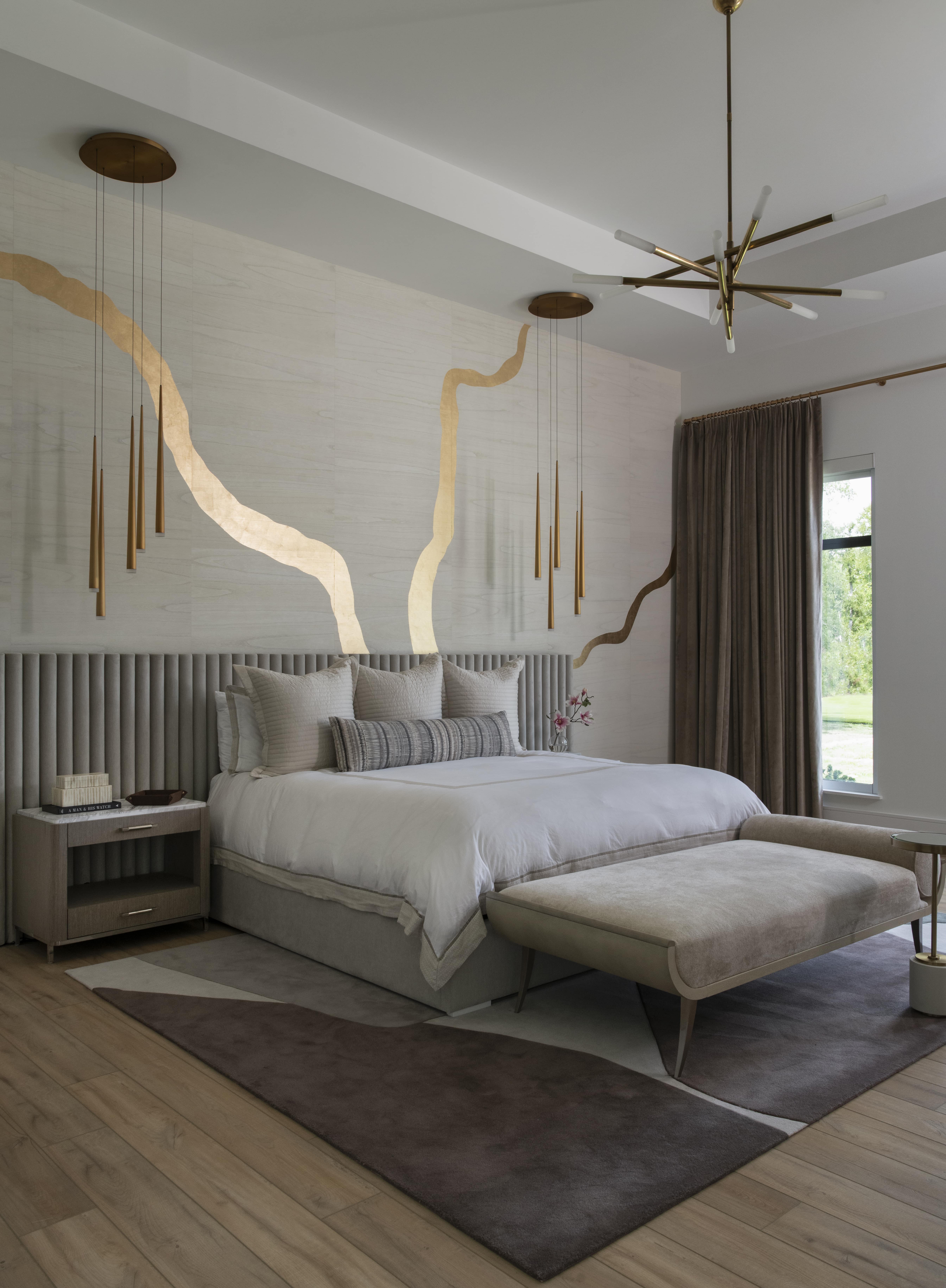 Bedroom with a gold-accented feature wall, upholstered bed, modern pendants, and layered neutral textiles.
