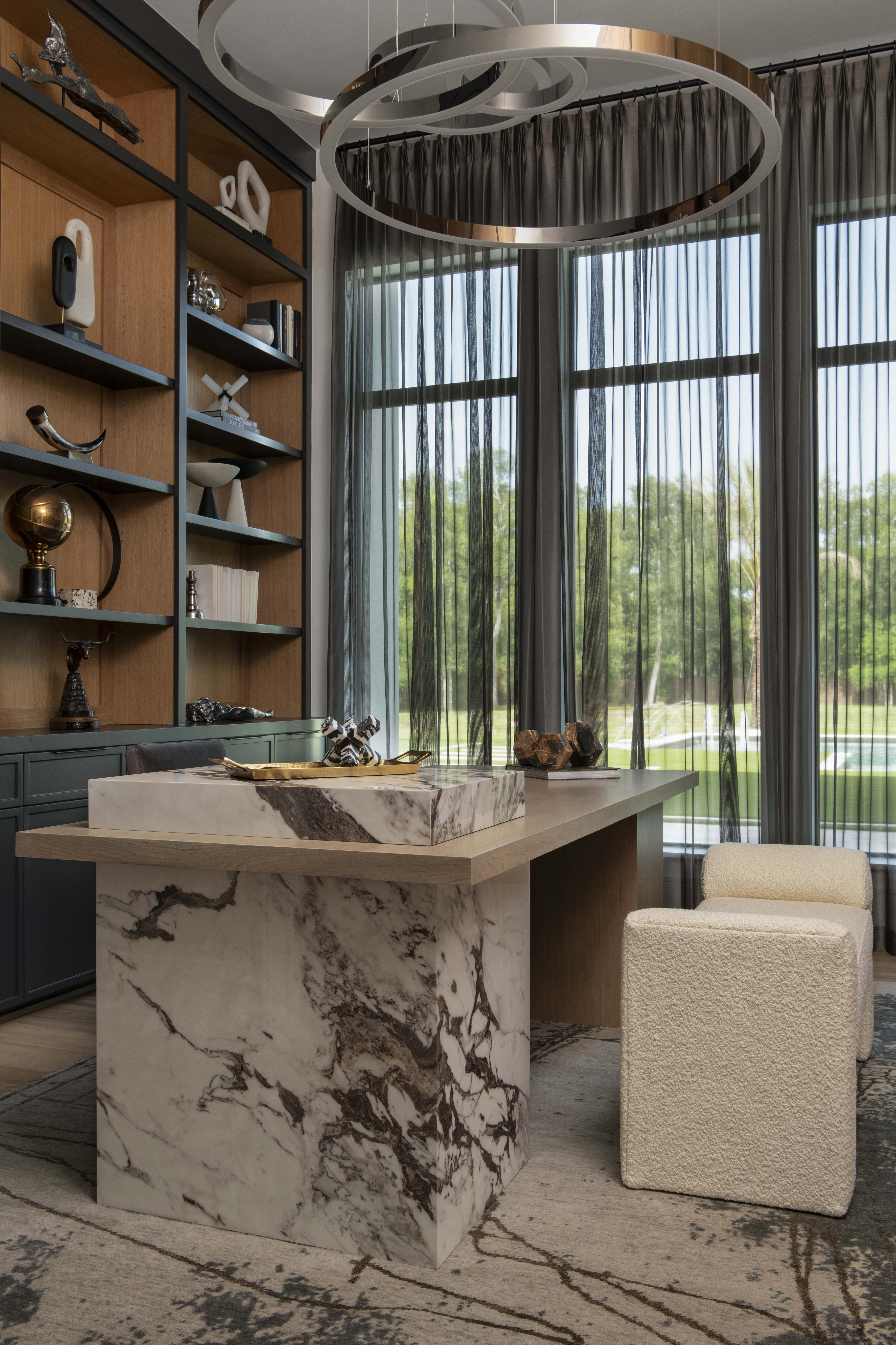 Home office with marble waterfall desk, tall built-ins, and sheer drapery framing views of the lawn.