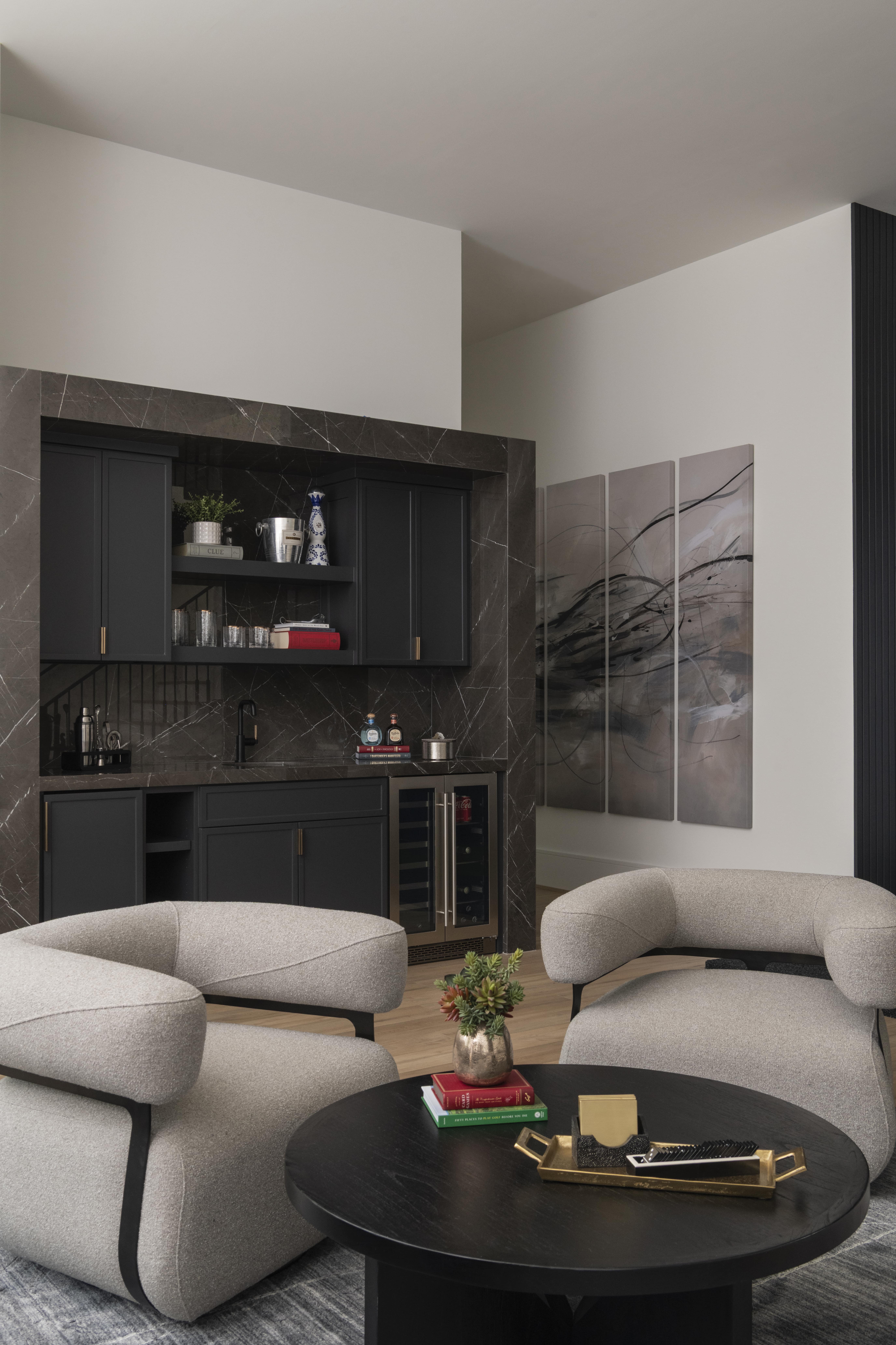 Lounge with sculptural gray chairs, dark round table, and a black bar framed in dramatic stone.