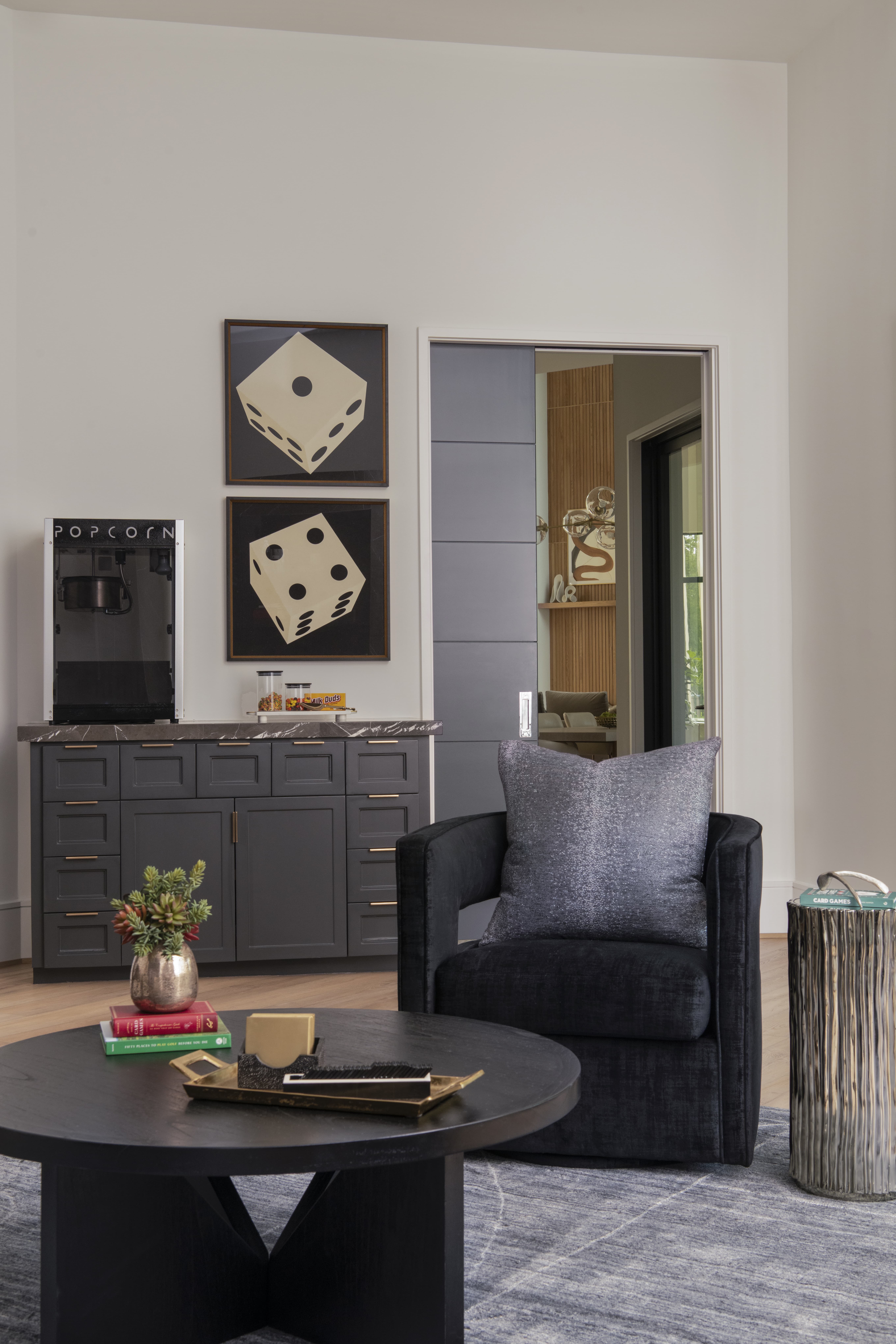 Game room with charcoal built-ins, popcorn machine, dice artwork, and cozy seating around a black round coffee table.