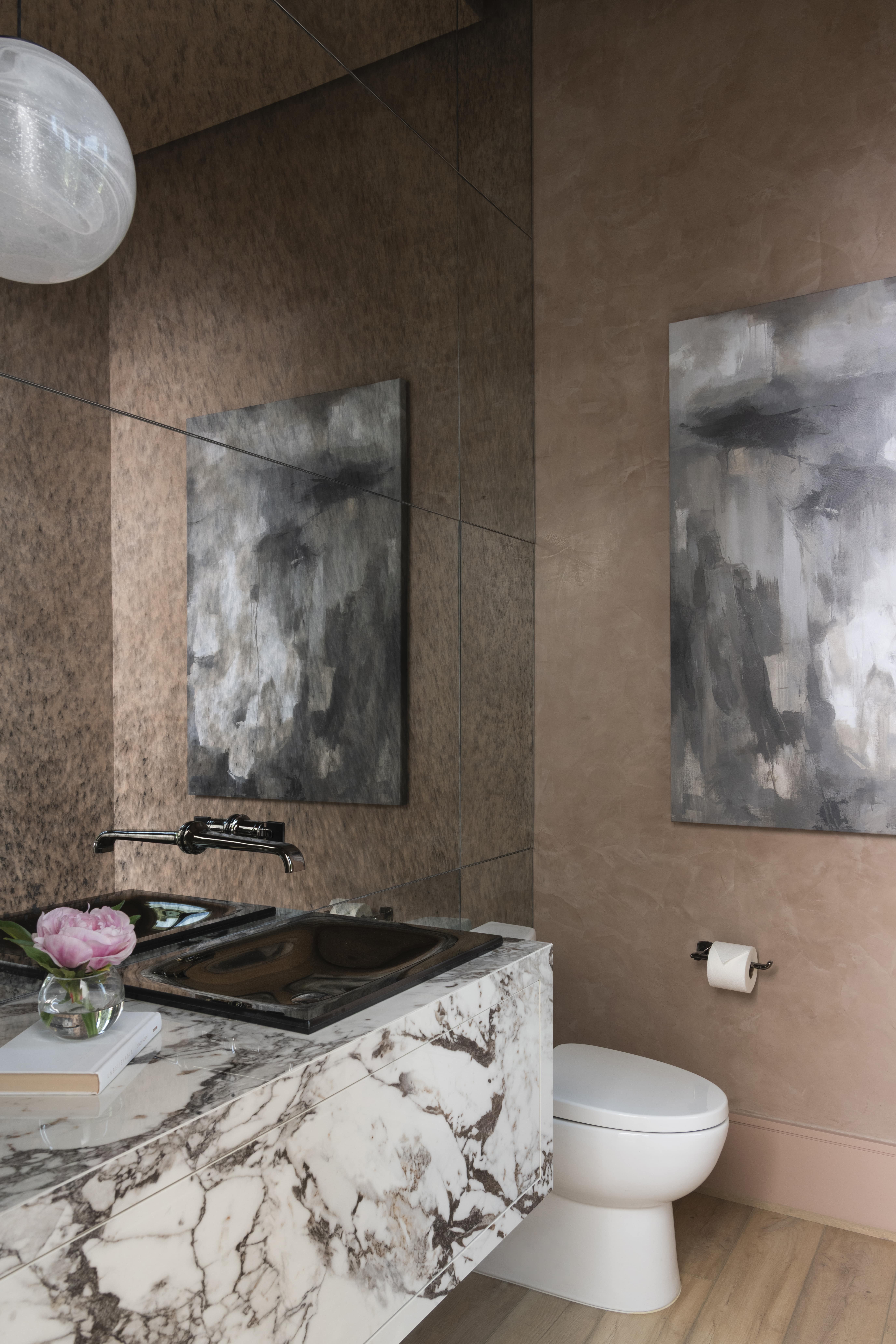 Powder bath with marble vanity, mirrored walls, and abstract artwork in soft earth tones.