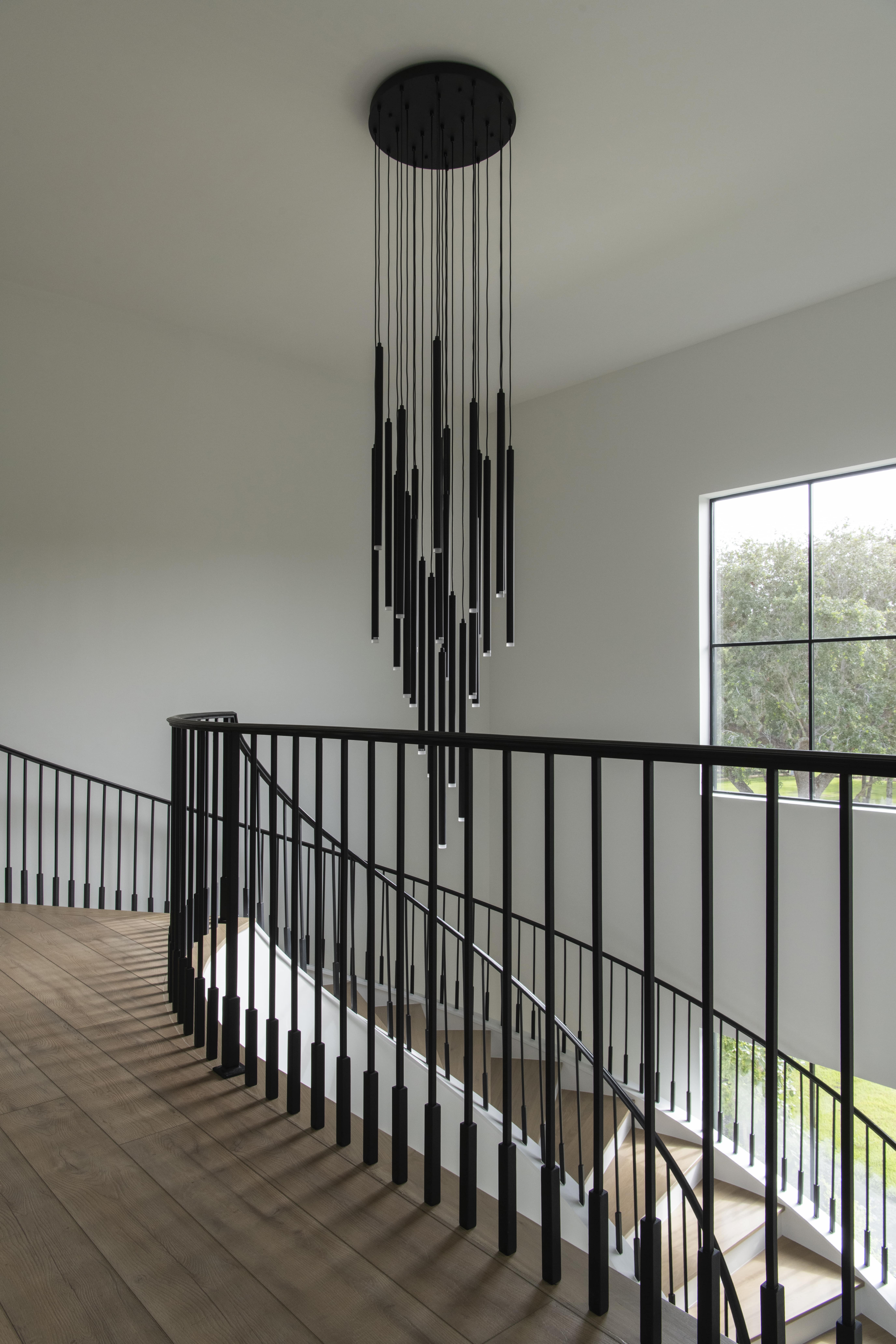 Modern staircase landing with a sculptural black multi-pendant chandelier and curved black railing overlooking wood floors.