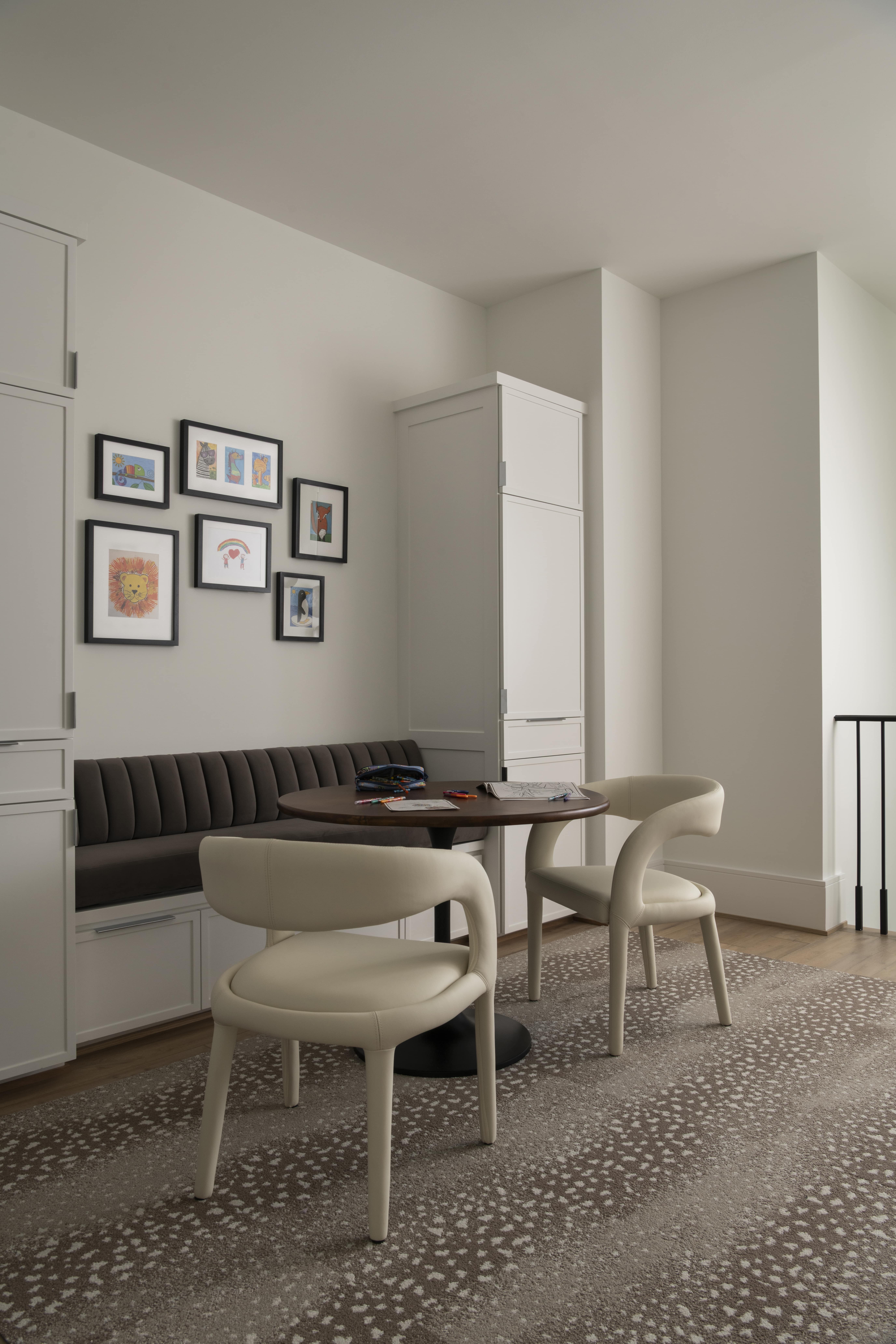 Cozy upstairs nook with built-in bench seating, round table, cream chairs, and framed children’s artwork on the wall.