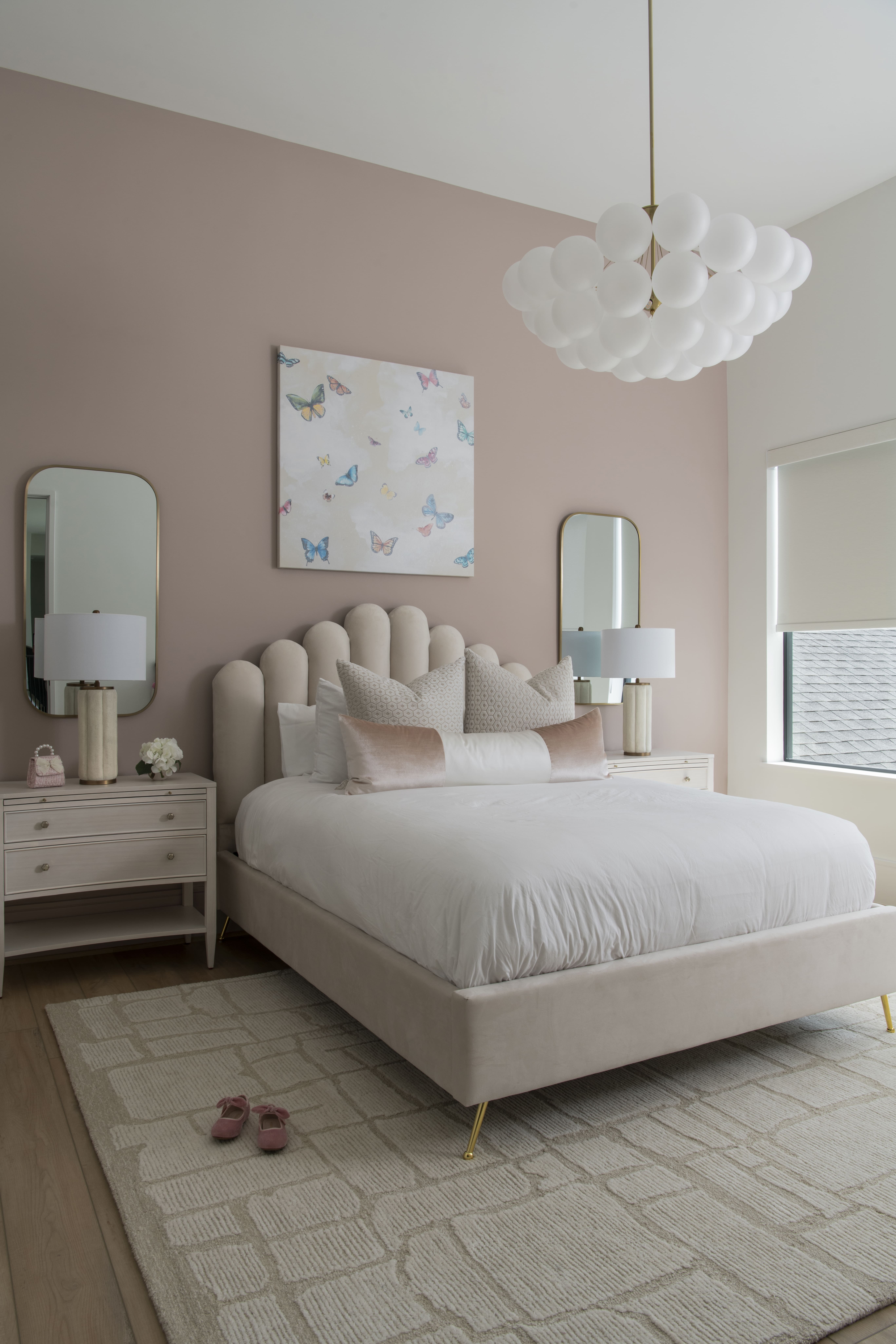 Soft blush bedroom with scalloped headboard, butterfly artwork, white bedding, and matching nightstands with lamps.