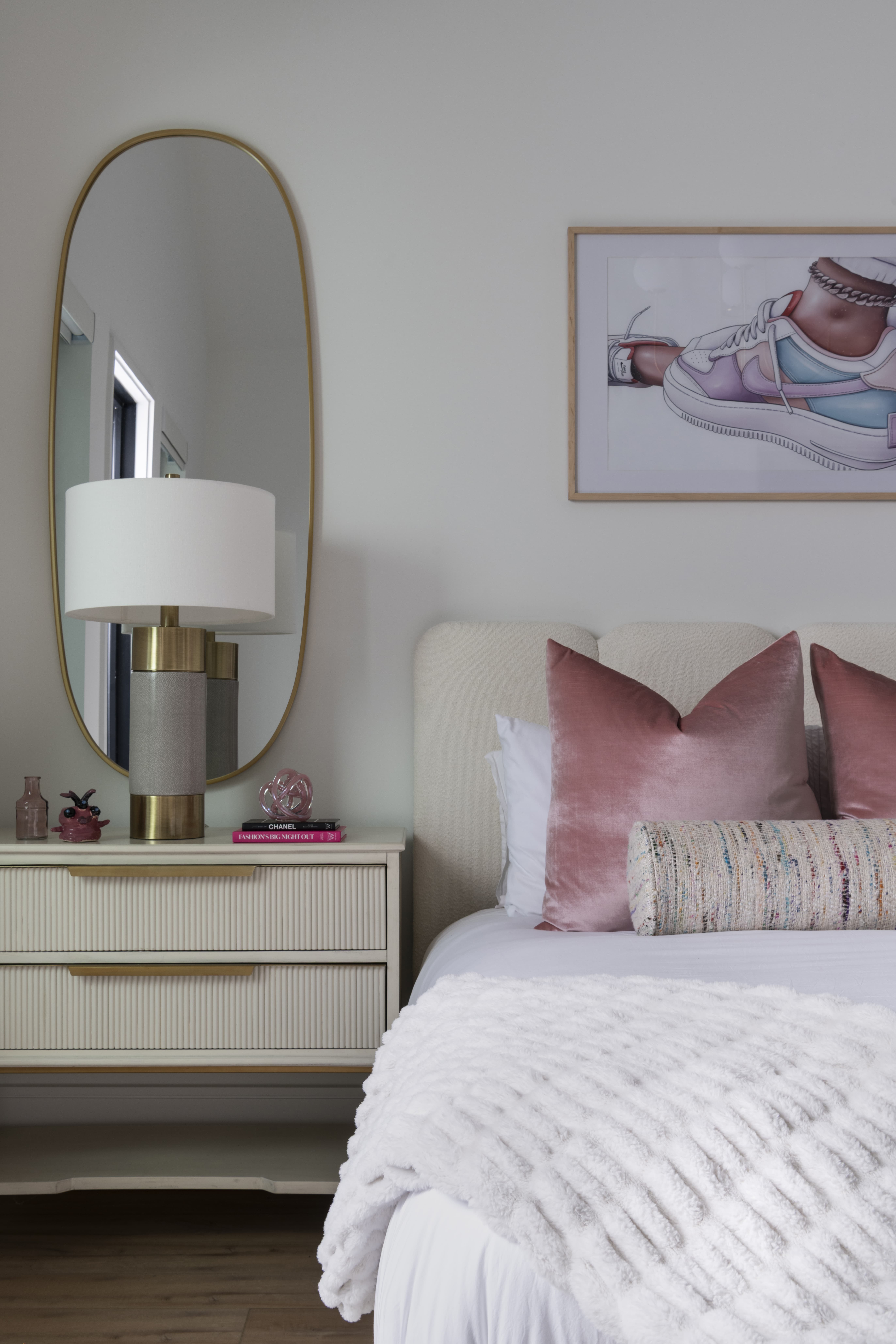 Stylish teen bedroom with framed sneaker artwork, pink velvet pillows, and a cream nightstand with brass-trimmed mirror.